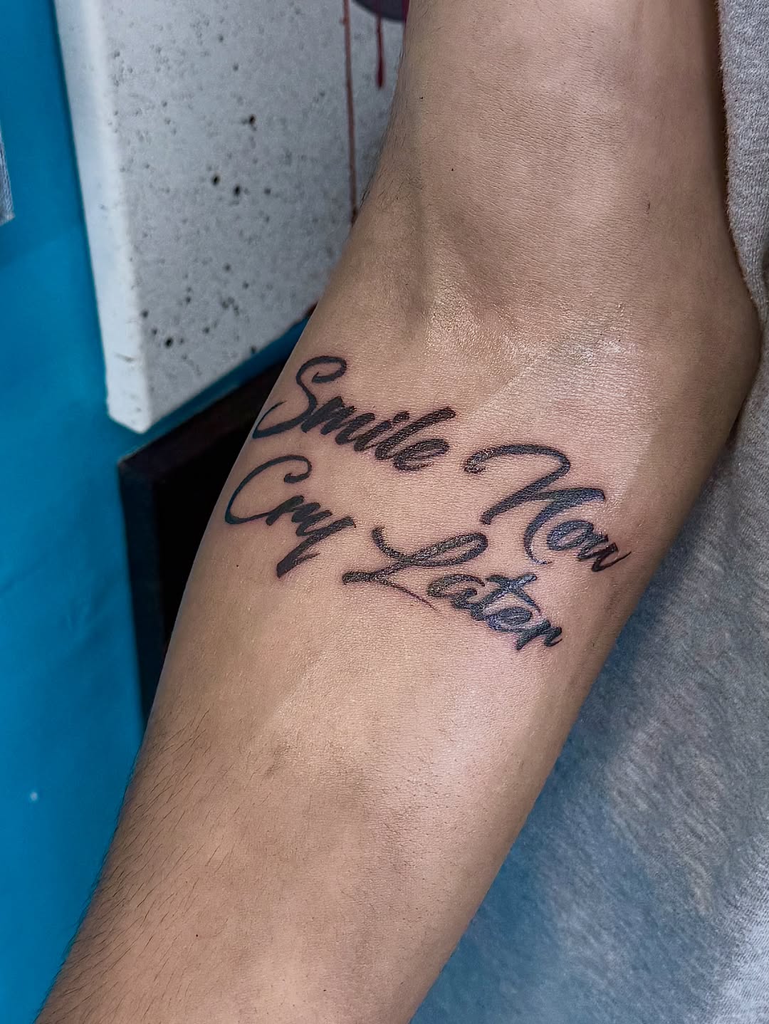 Smile Now Cry Later script lettering tattoo on the forearm by ⠀Greave