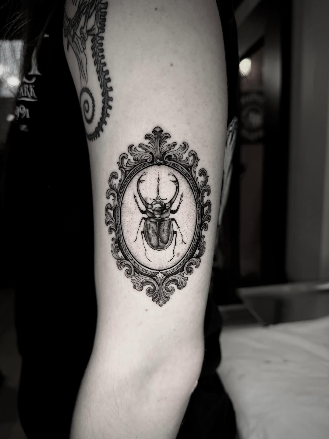 Ornate framed beetle fine line tattoo on the forearm by Ingrid Rojas
