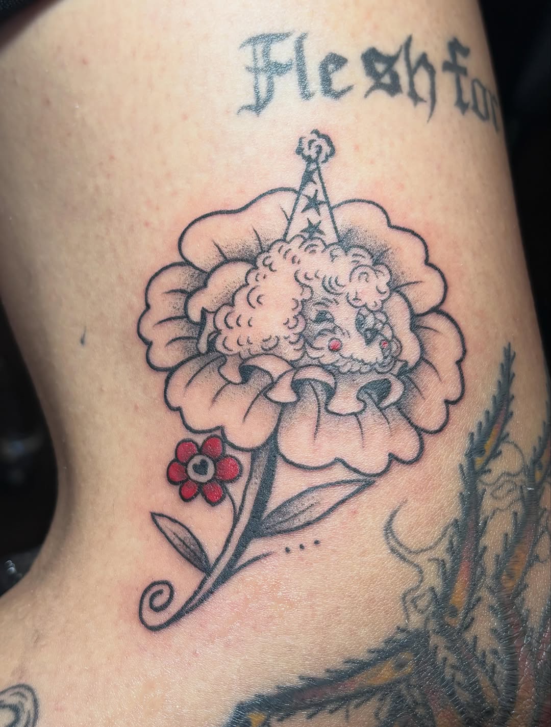 Dog in flower with party hat ignorant tattoo on the thigh by Sasha “Sashimi” Shabasov