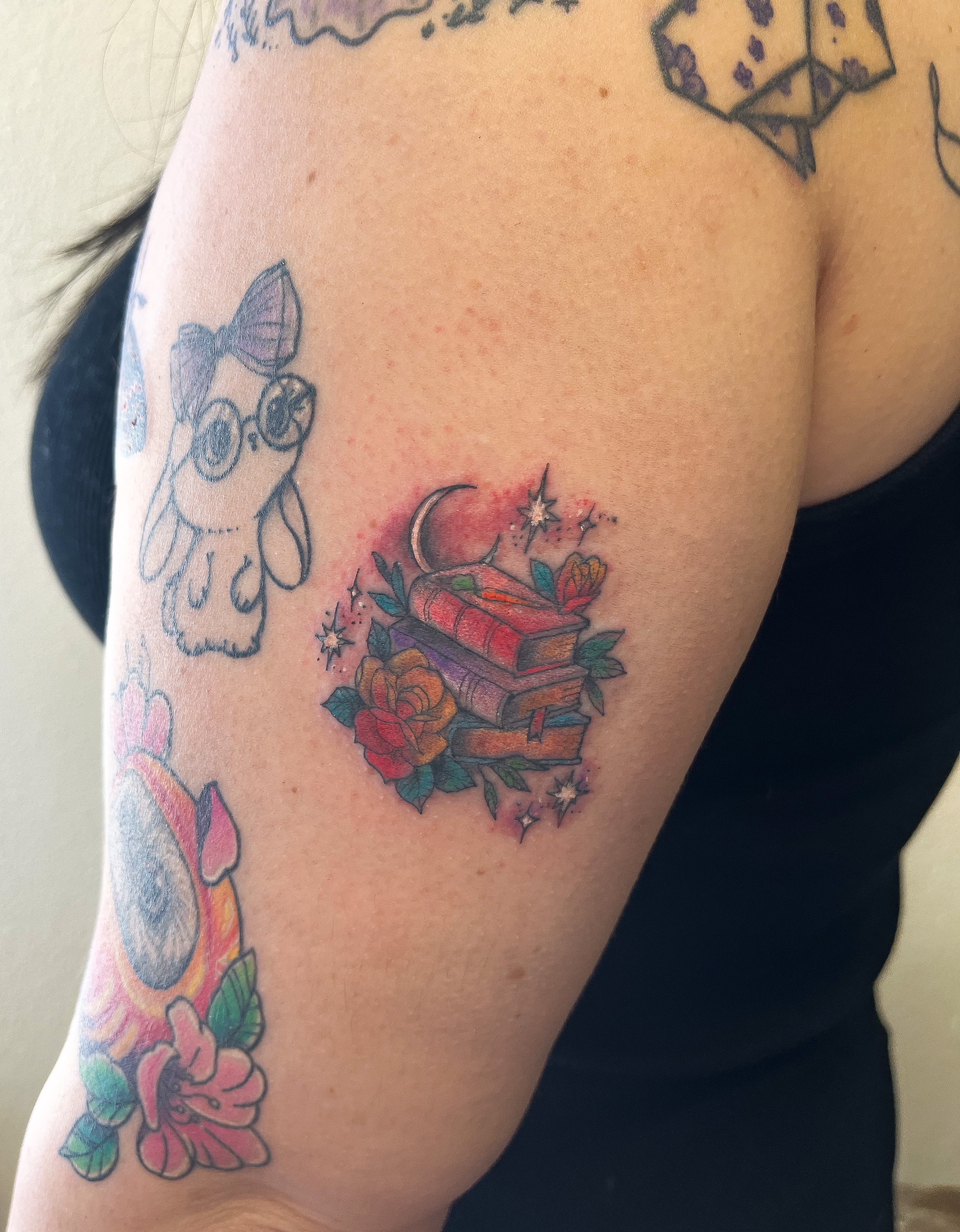 Books and flowers American traditional tattoo on the upper arm by Janelle Cuba