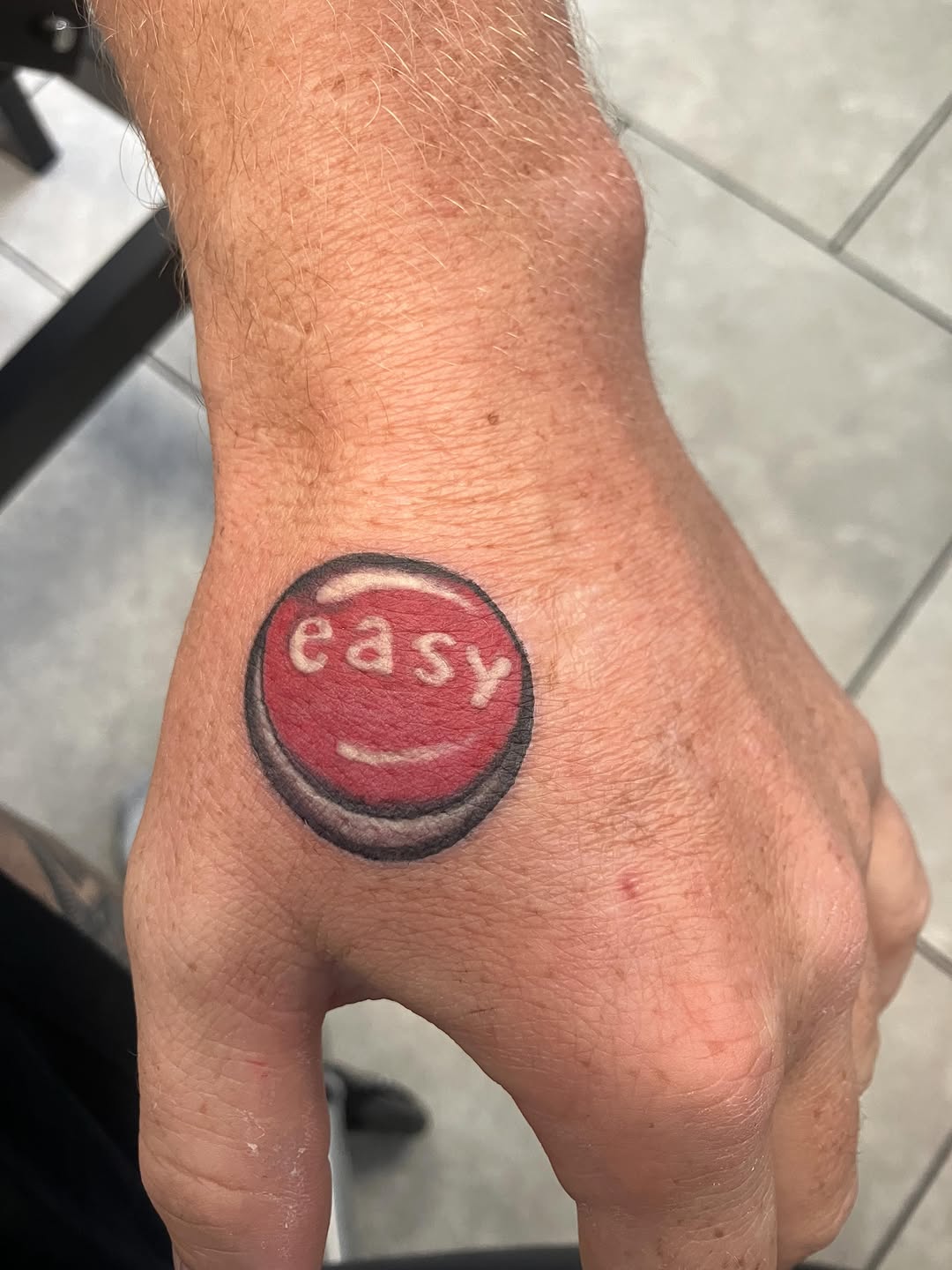 Red button with 'easy' text tattoo on the hand by Bryant Johnson