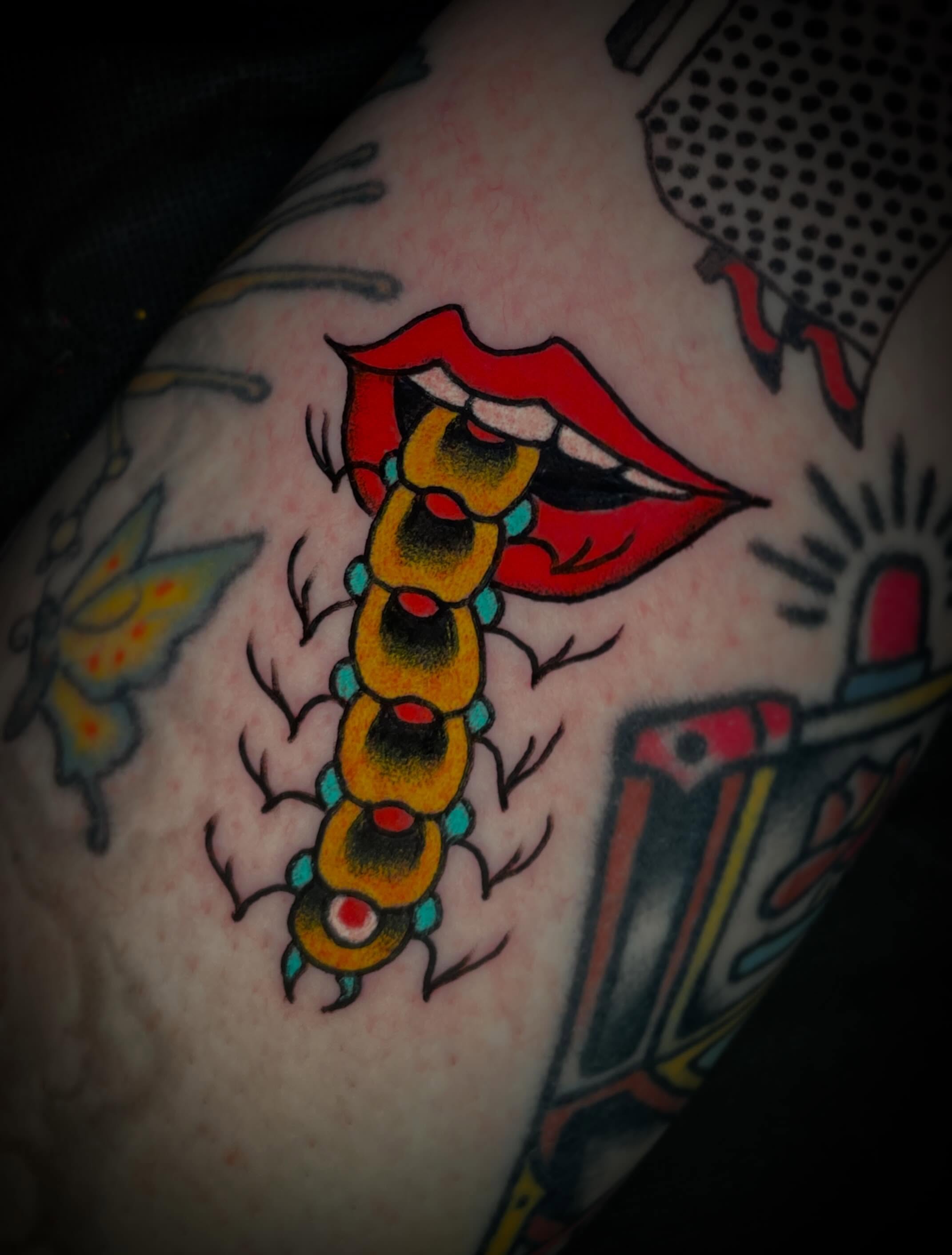 Lips and centipede American traditional tattoo on the upper arm by Nick Wallin