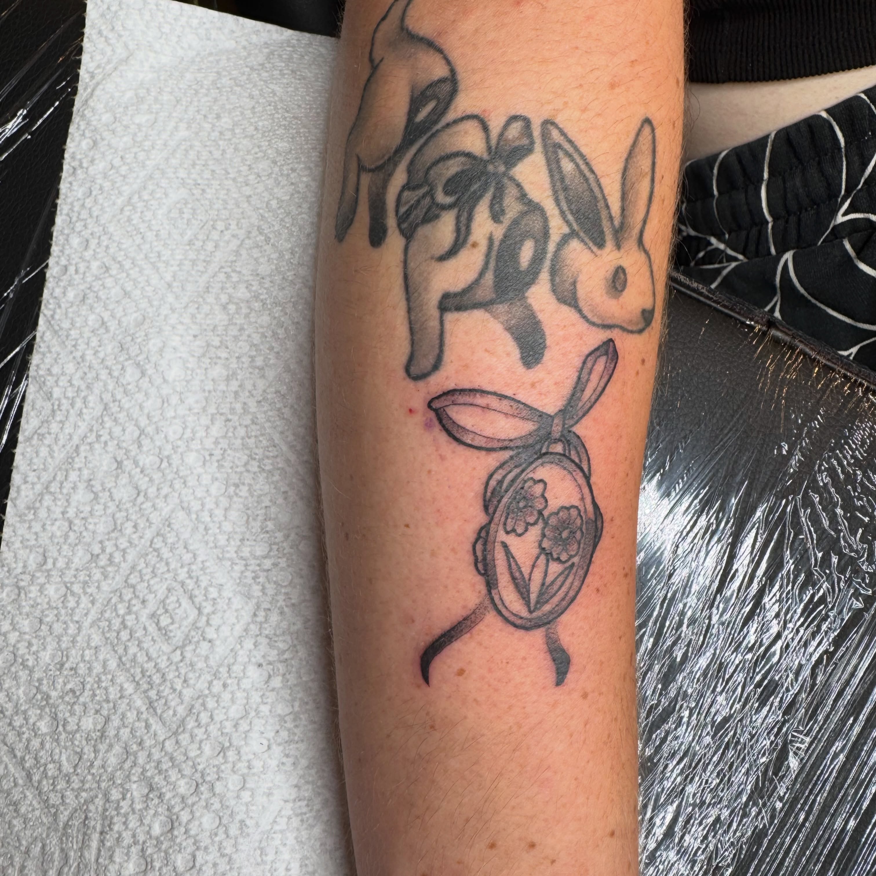 Rabbit and locket black and grey tattoo on the forearm by tori 🫶🏻