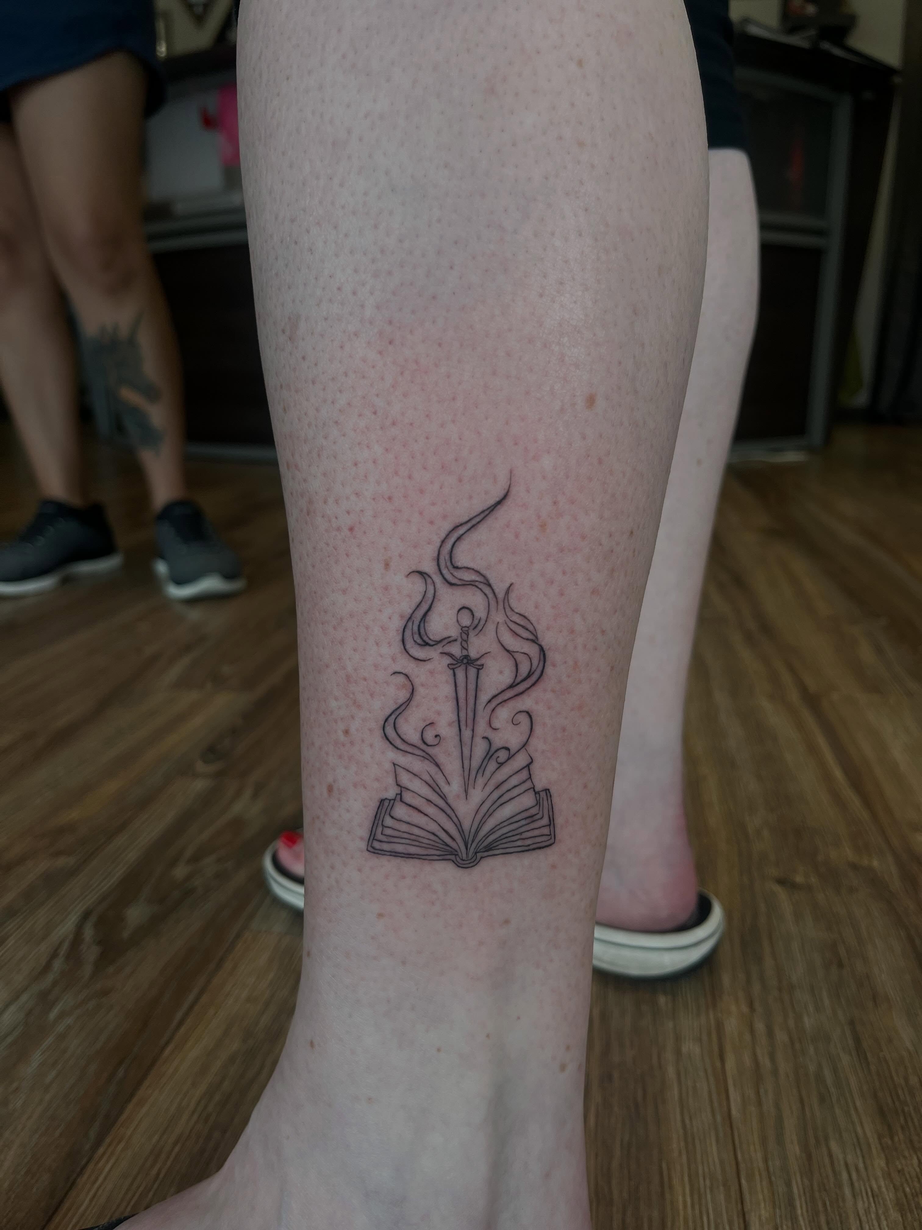 Book and sword black and grey tattoo on the calf by Cass