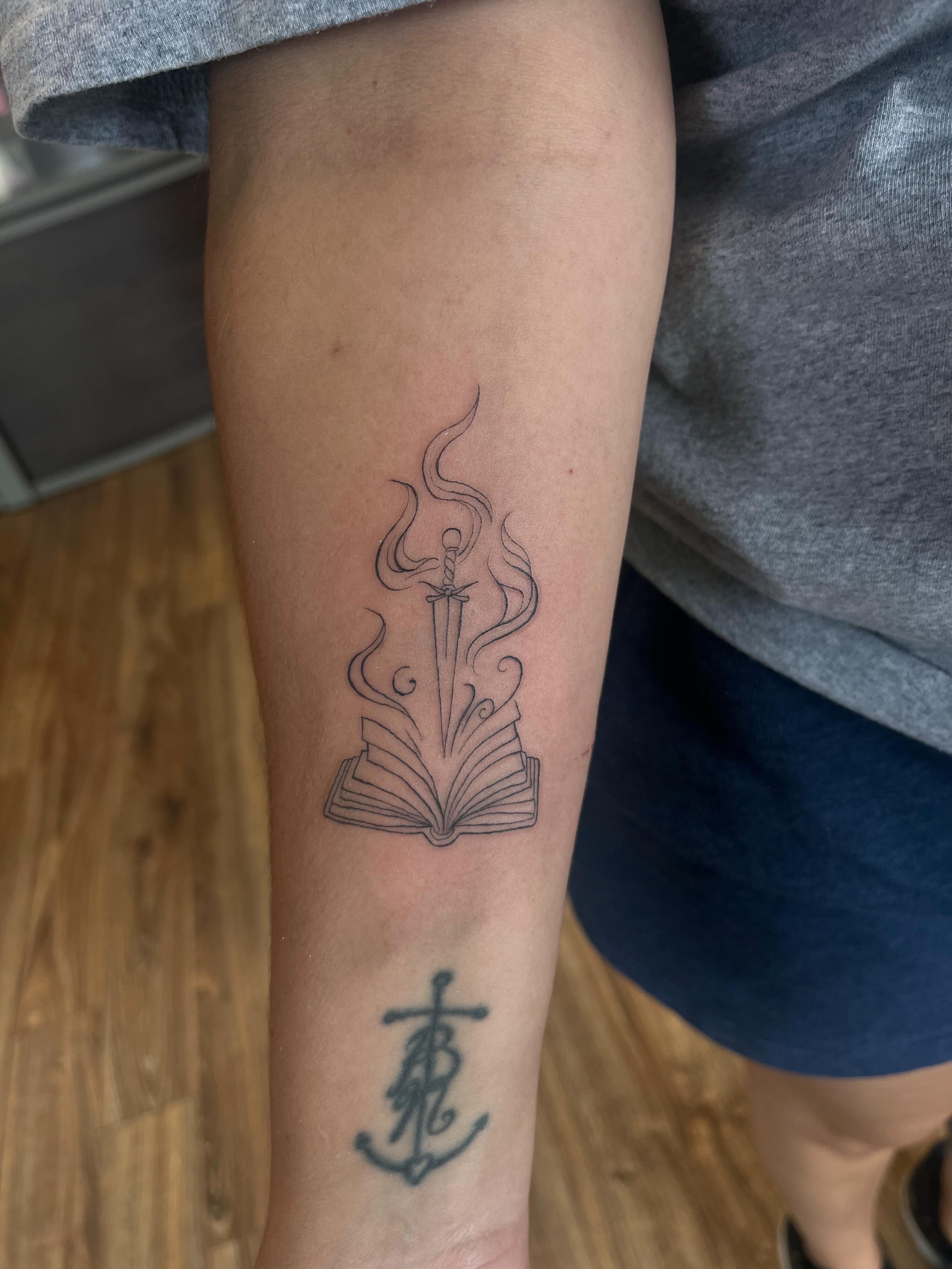 Book and sword black and grey tattoo on the forearm by Cass
