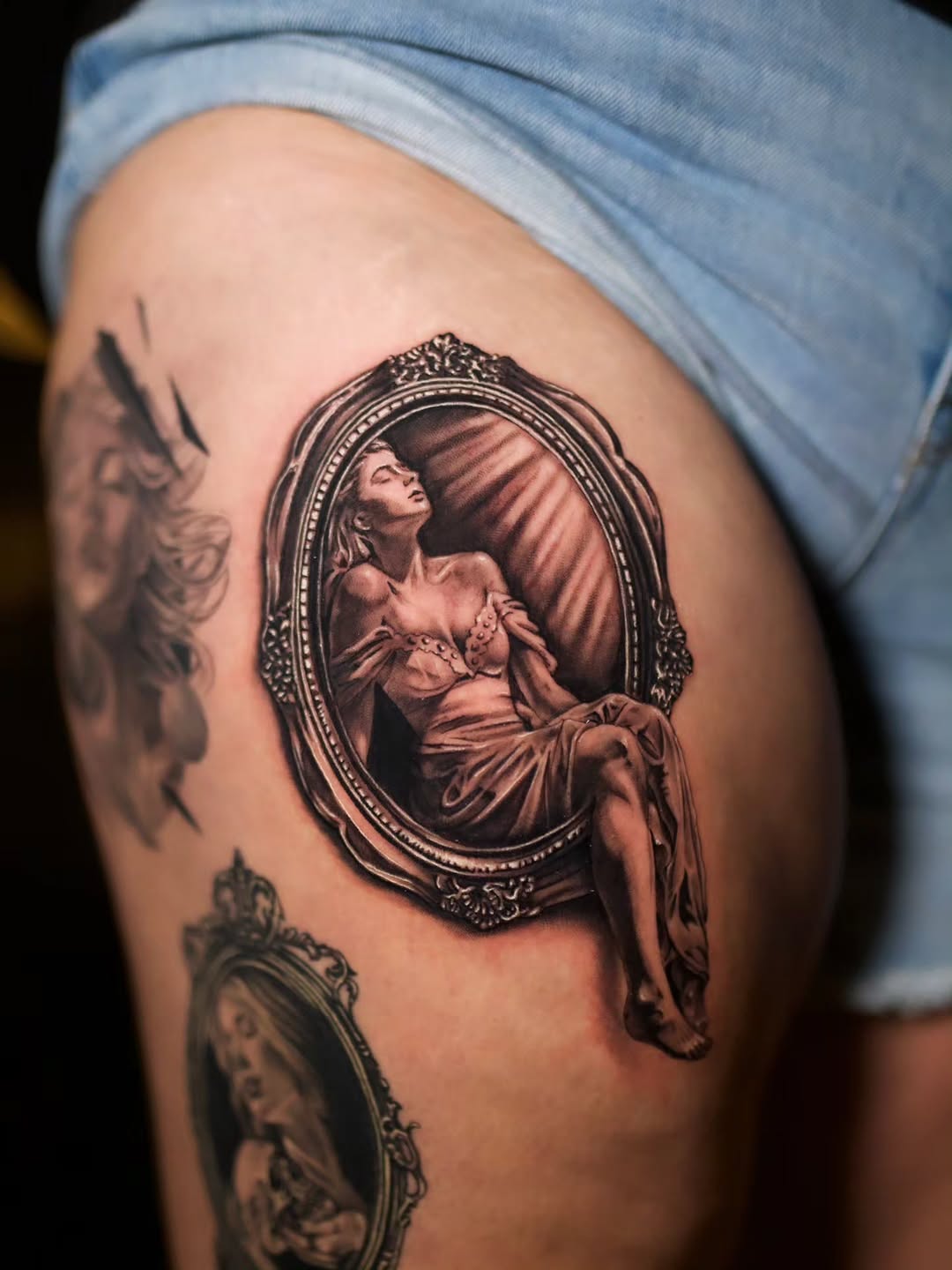 Woman in ornate mirror frame realism tattoo on the thigh by Jake Barney
