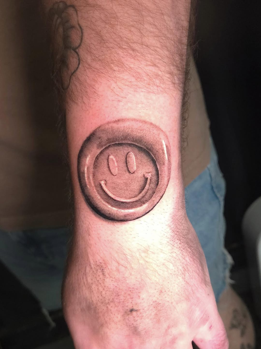 Smiley face button ignorant tattoo on the forearm by Maya Neideck