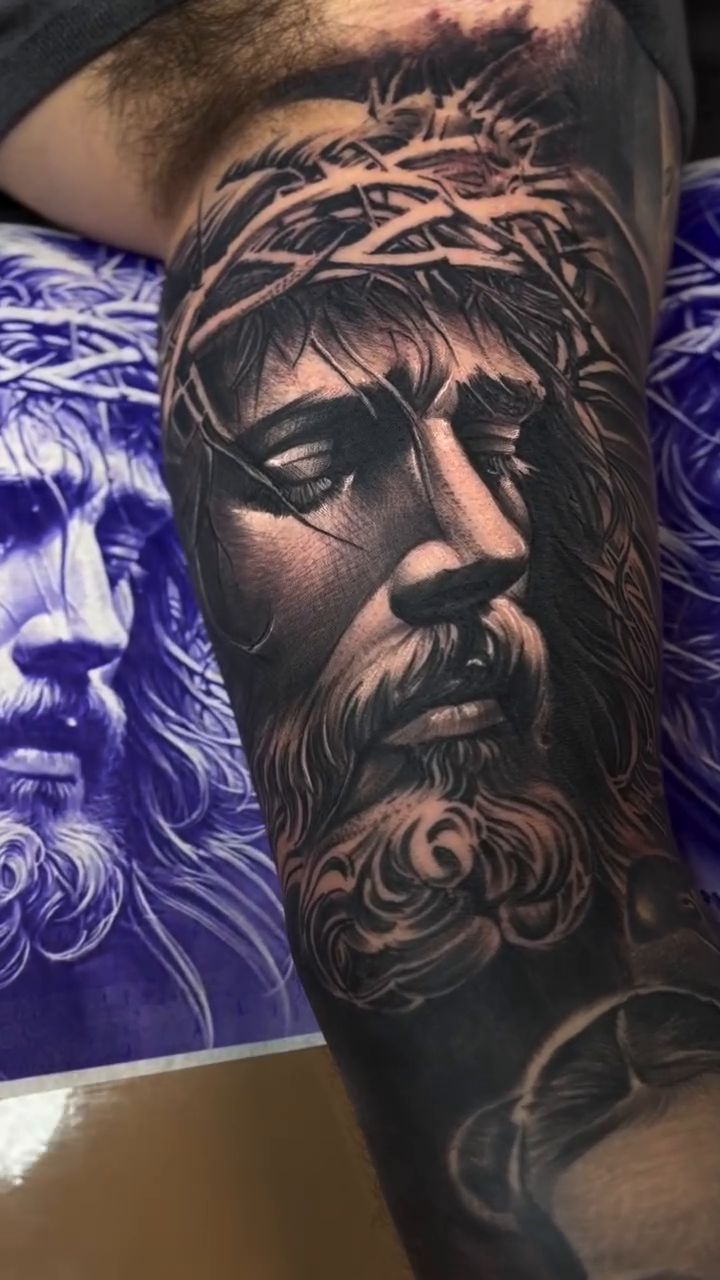 Jesus Christ portrait with a baby Chicano tattoo on the forearm by Raul Rodriguez