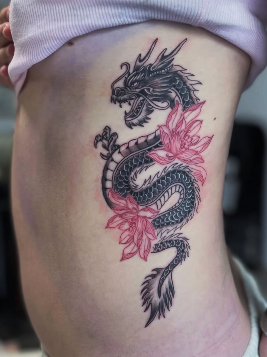 Dragon with lotus flowers watercolor tattoo on the thigh by @elijahtats