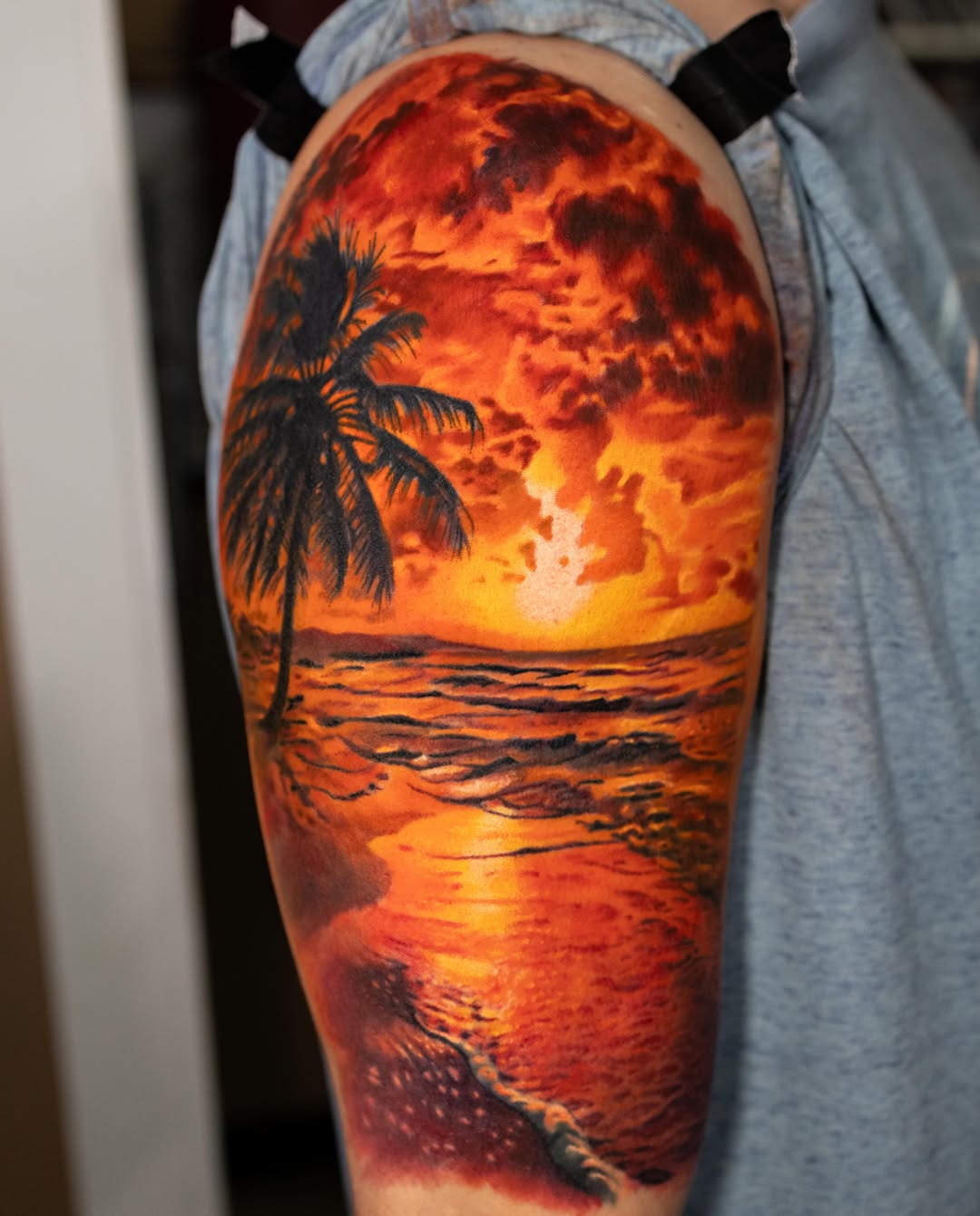 Sunset beach scene with palm tree realism tattoo on the upper arm by Realistic tattoos in Minneapolis, MN, Minneapolis, Minnesota