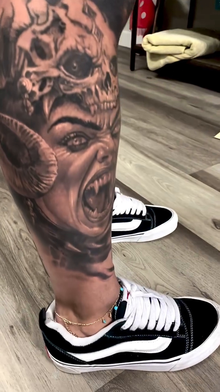 Demon face and skulls with text realism tattoo on the calf by David Garner, Los Angeles, California