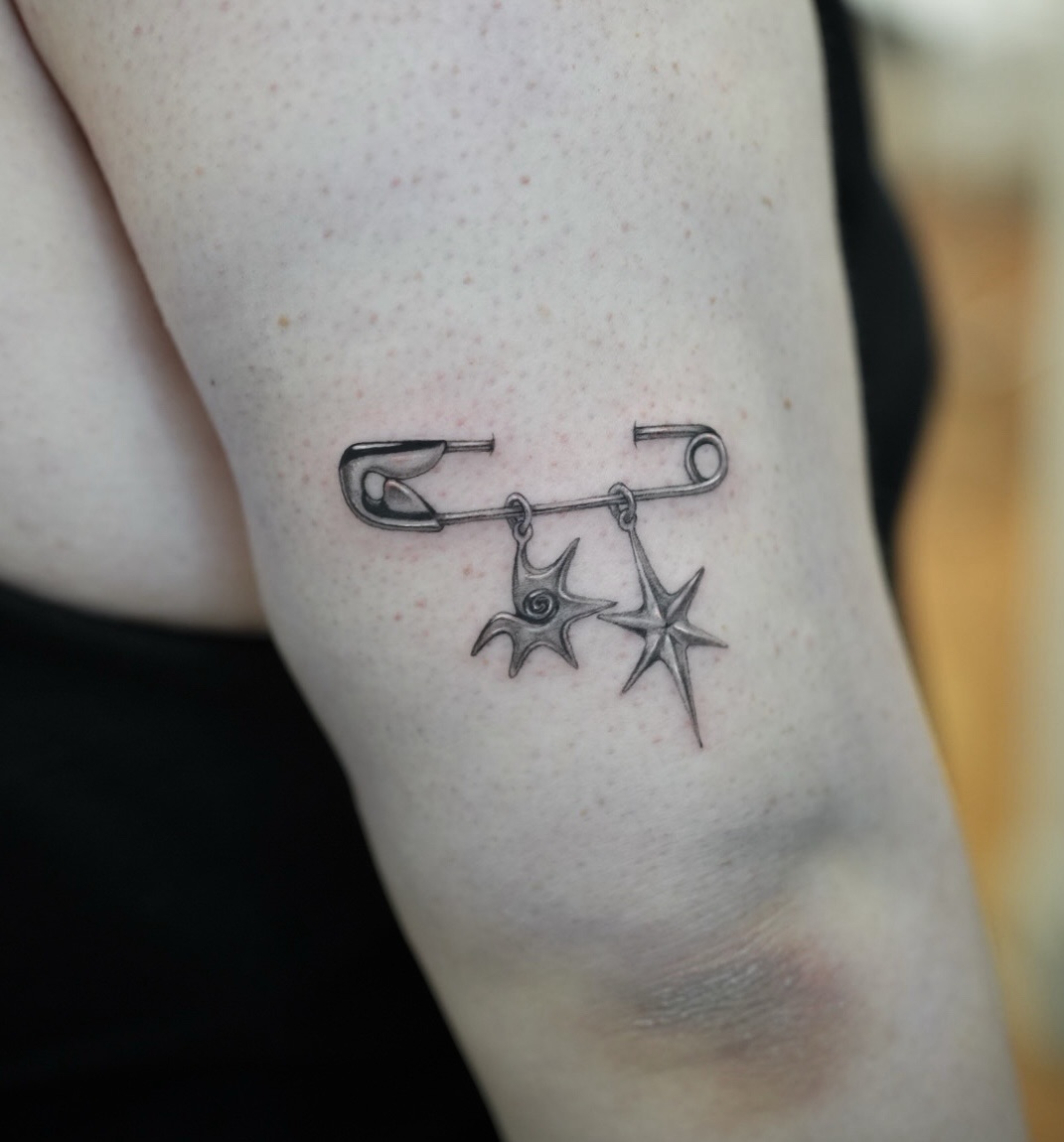Safety pin with charms minimalist tattoo on the forearm by Hery Anwar