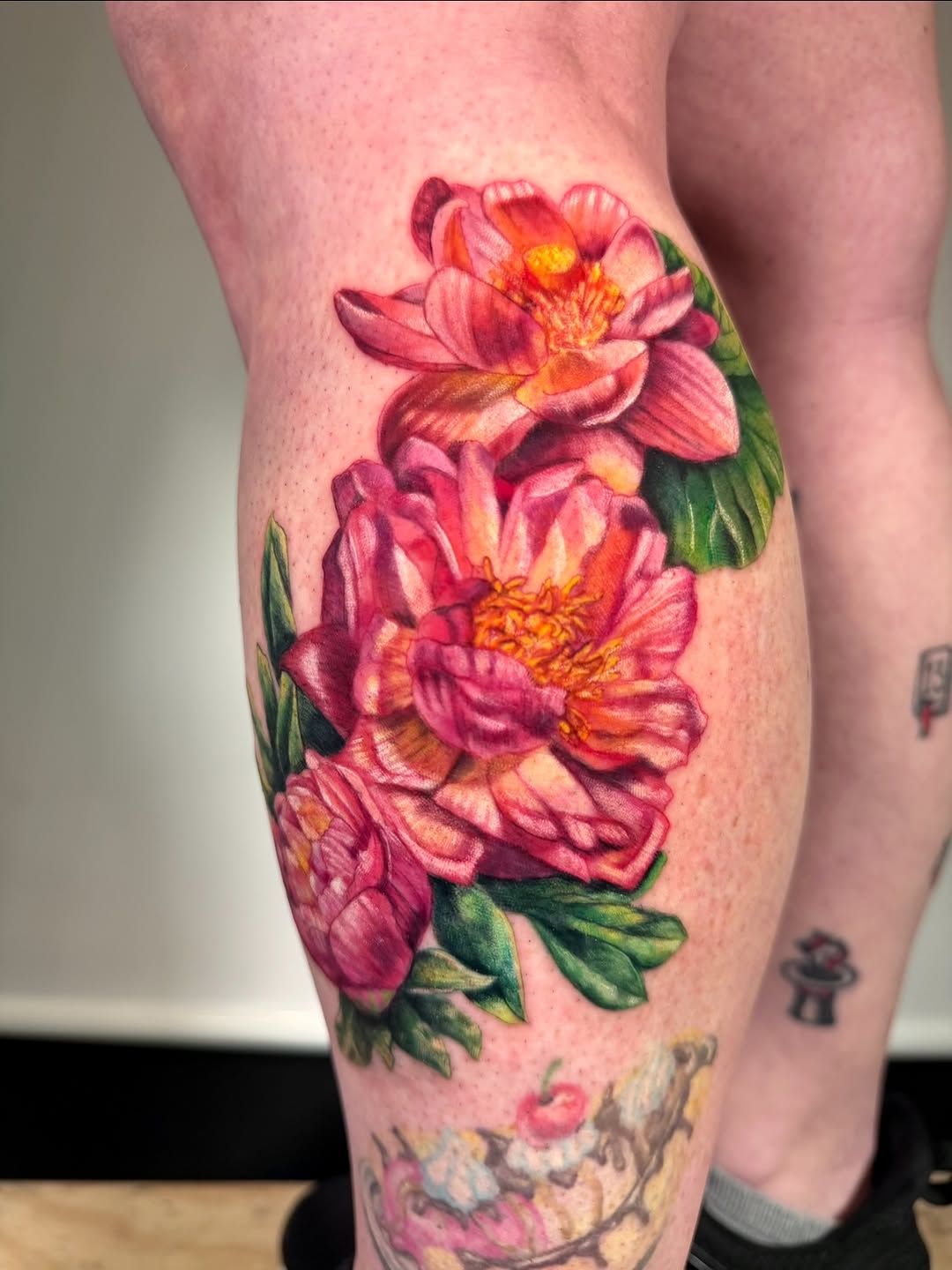 Pink flowers with green leaves neo-traditional tattoo on the calf by aria, Austin, Texas