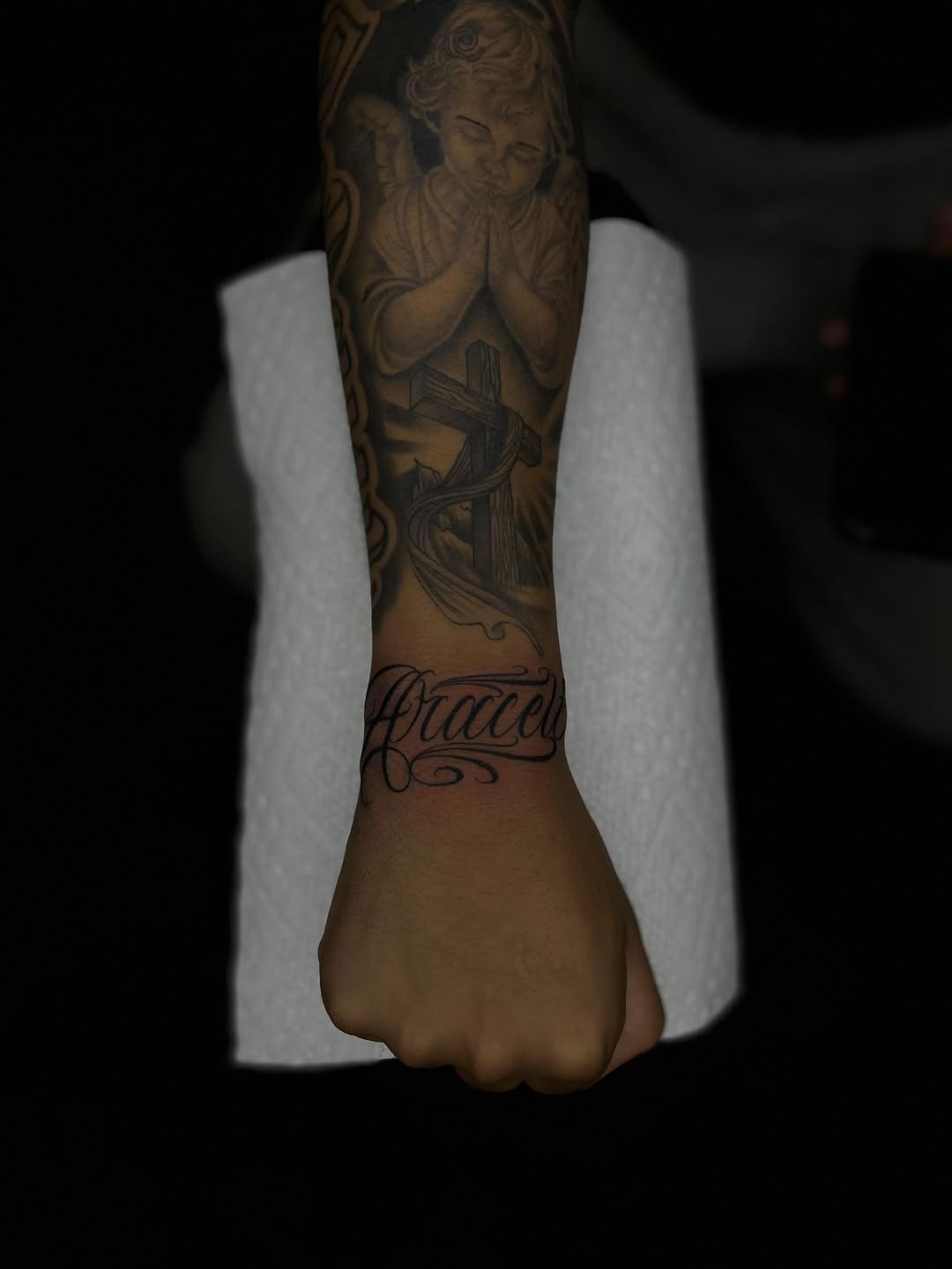 Angel, cross, and script lettering Chicano tattoo on the forearm by Tattoo Artist