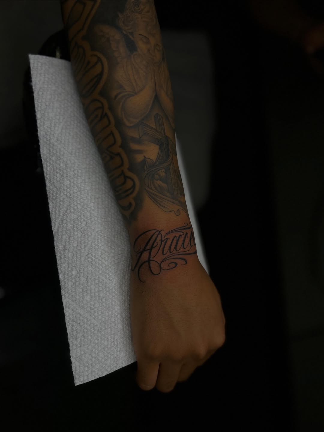 Angel and cross with lettering lettering tattoo on the forearm by Tattoo Artist