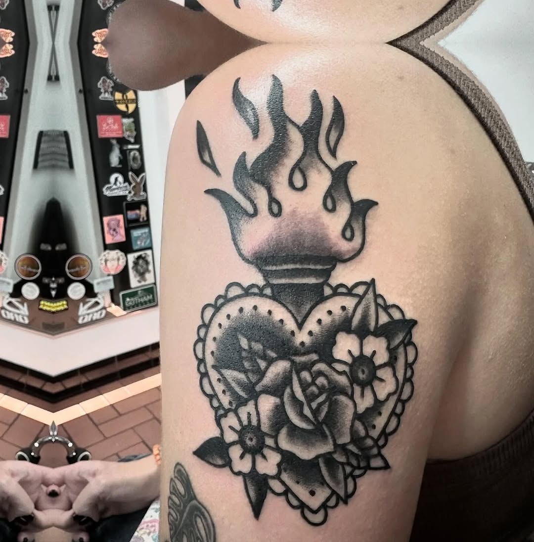 Heart with flames and flowers American traditional tattoo on the shoulder by Greyson Heidenreich