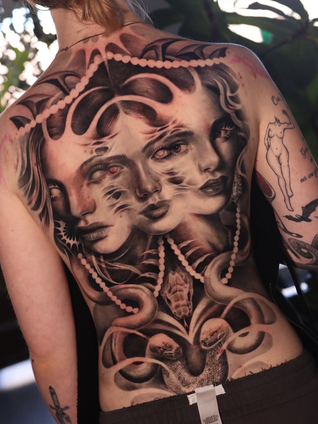 Multiple faces and snakes surrealism tattoo on the back by Naomi Burke, New Westminster, British Columbia