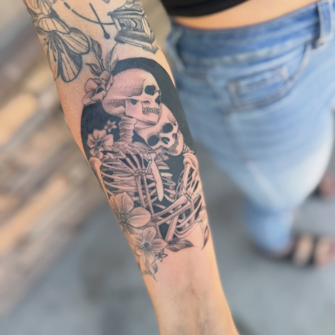 Skeletons and flowers black and grey tattoo on the forearm by Faith Lopez