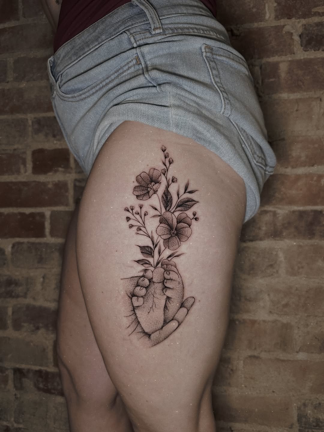 Baby feet holding flowers fine line tattoo on the thigh by E L I Z A H B e T H H D e S I G N S