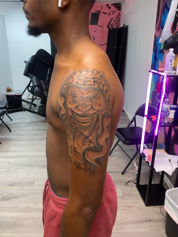 Joker face with text realism tattoo on the upper arm by Mariš¤, Chicago, Illinois