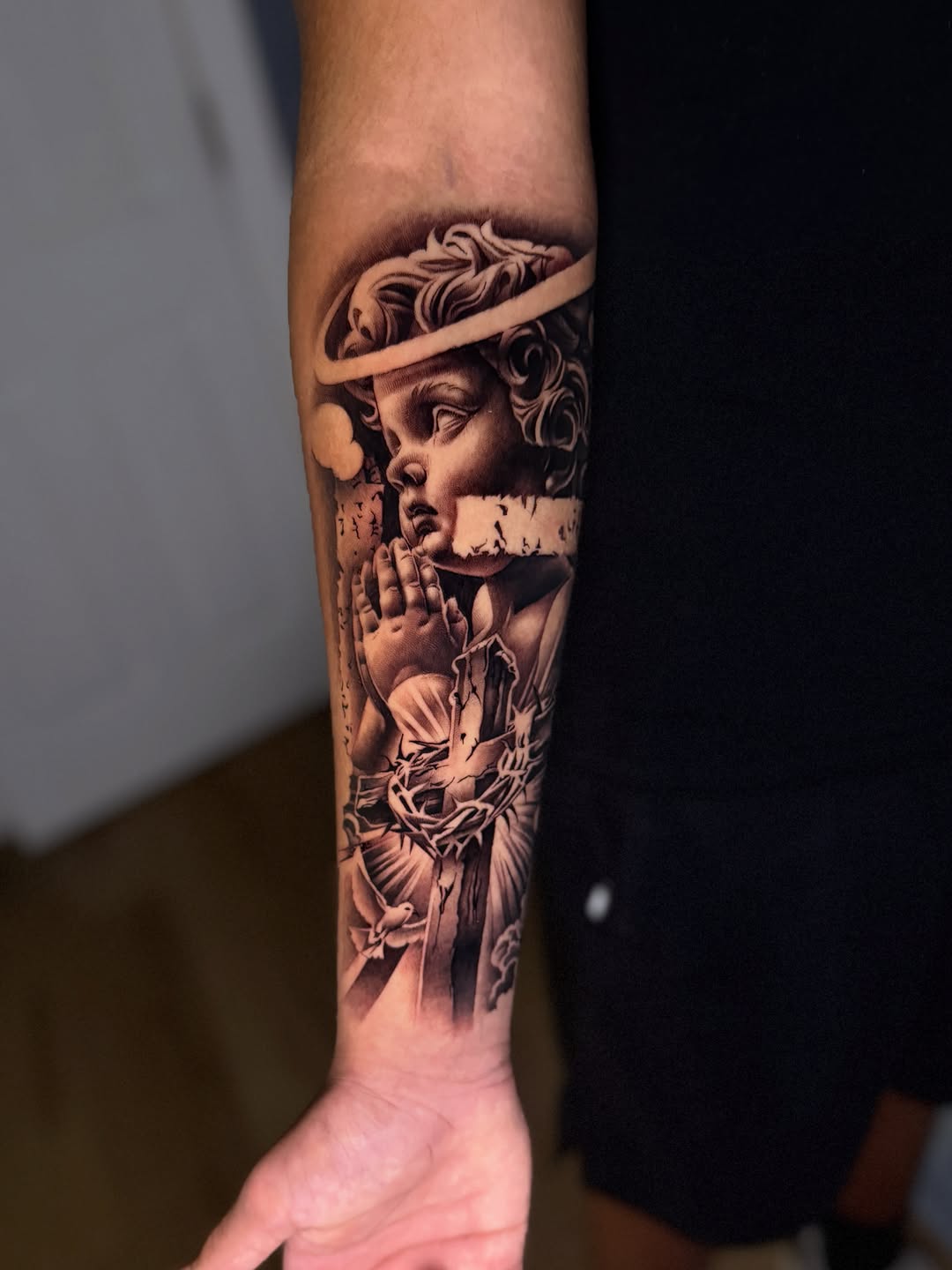 Cherub with cross and dove realism tattoo on the forearm by Miles Johnson