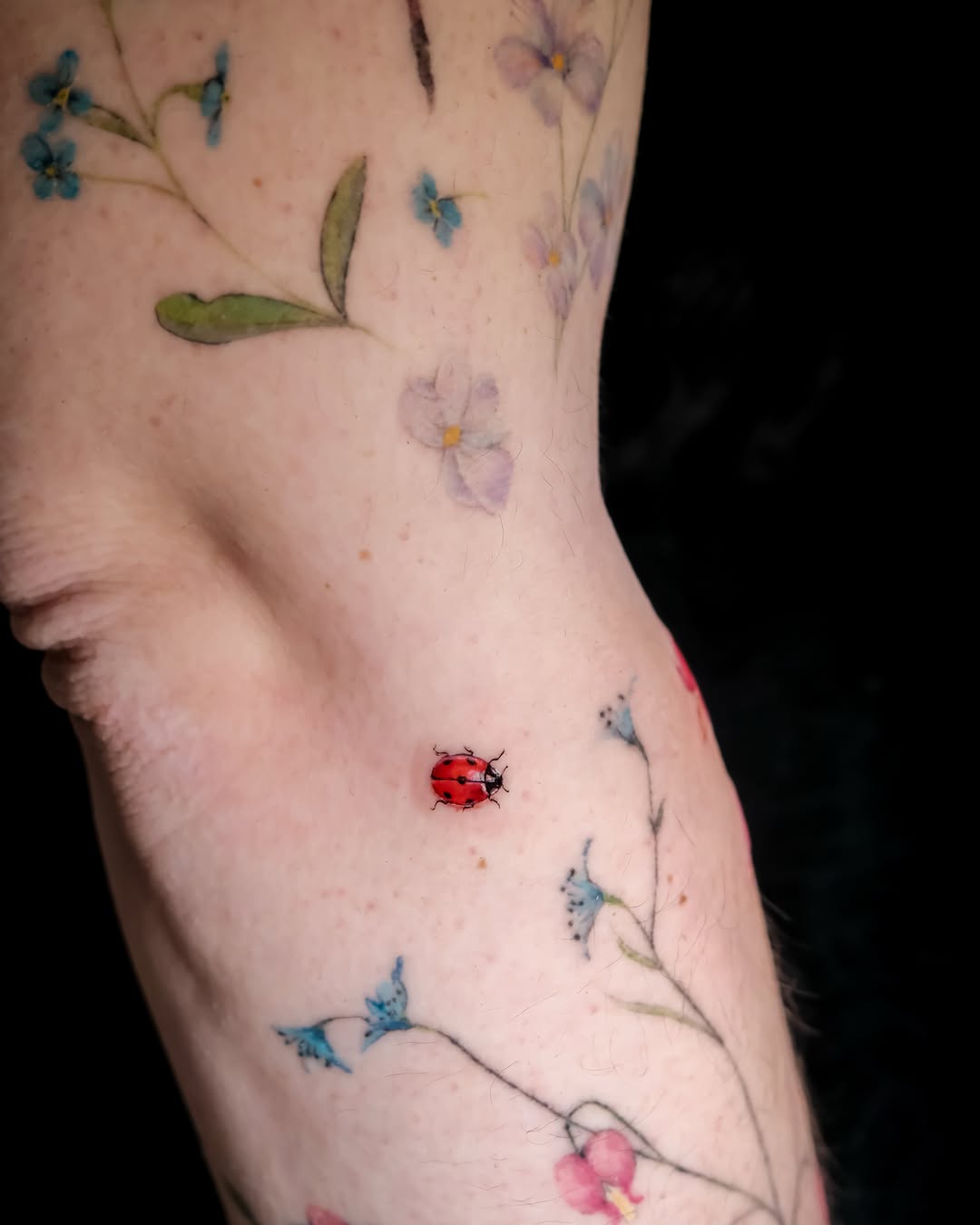 Ladybug and flowers watercolor tattoo on the forearm by NAS