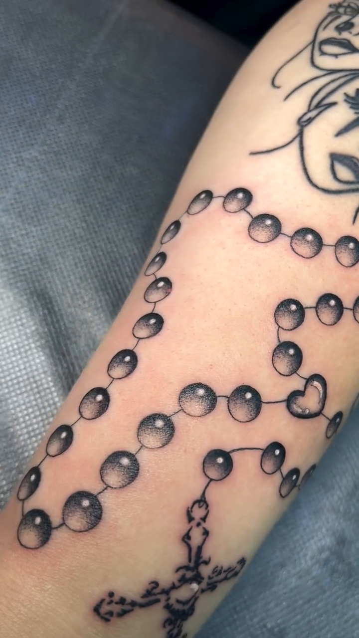 Rosary beads with cross lettering tattoo on the forearm by christina diaz