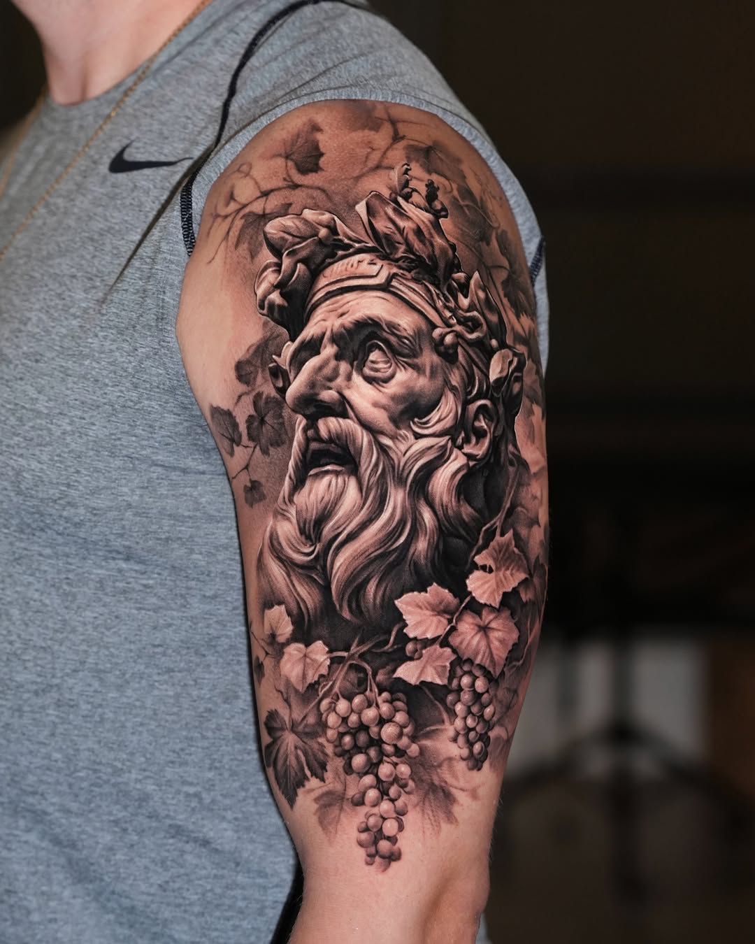 Bust of a man with grapes surrealism tattoo on the upper arm by Gody