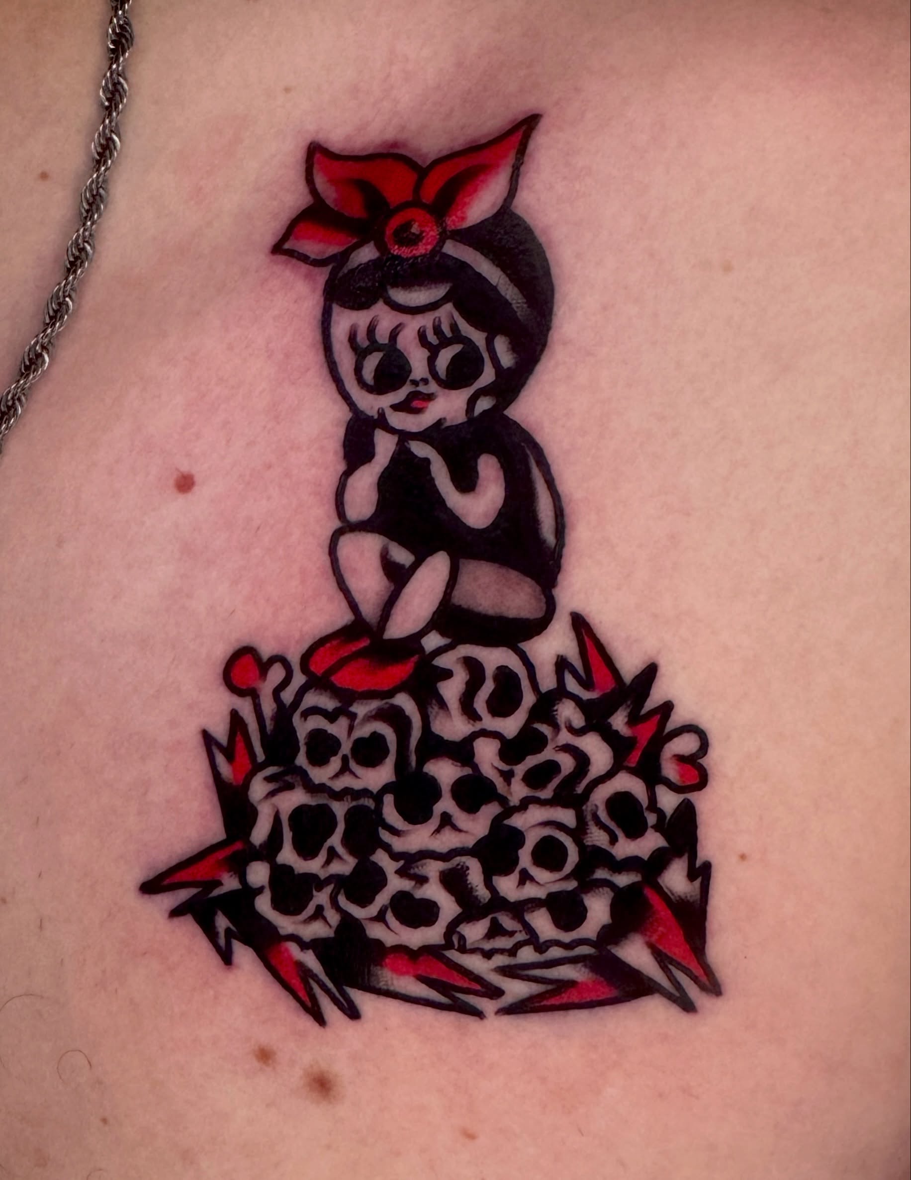 Doll surrounded by skulls American traditional tattoo on the torso by Butz Tattoos