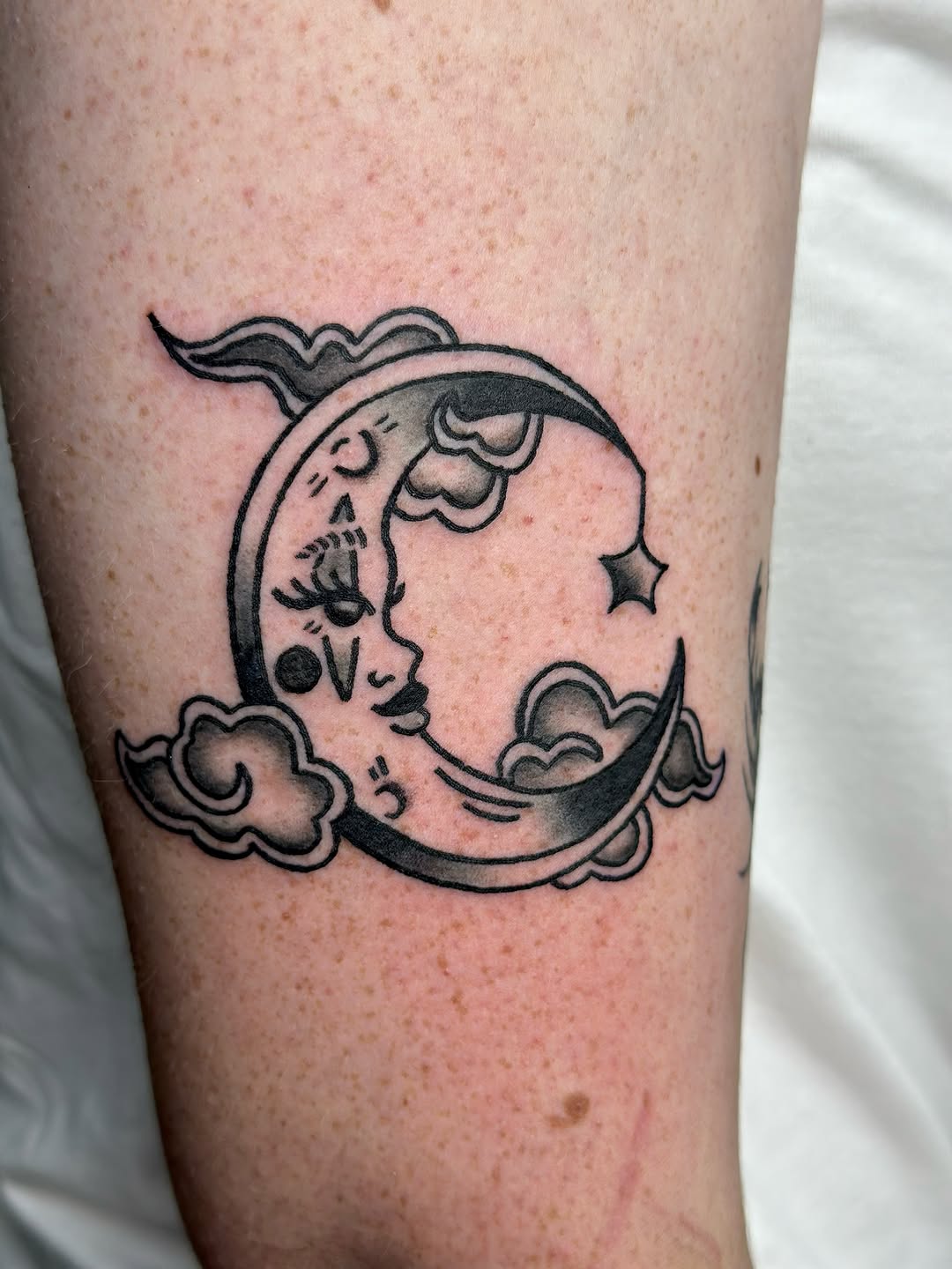 Crescent moon with face and clouds fine line tattoo on the forearm by Lucy Jay