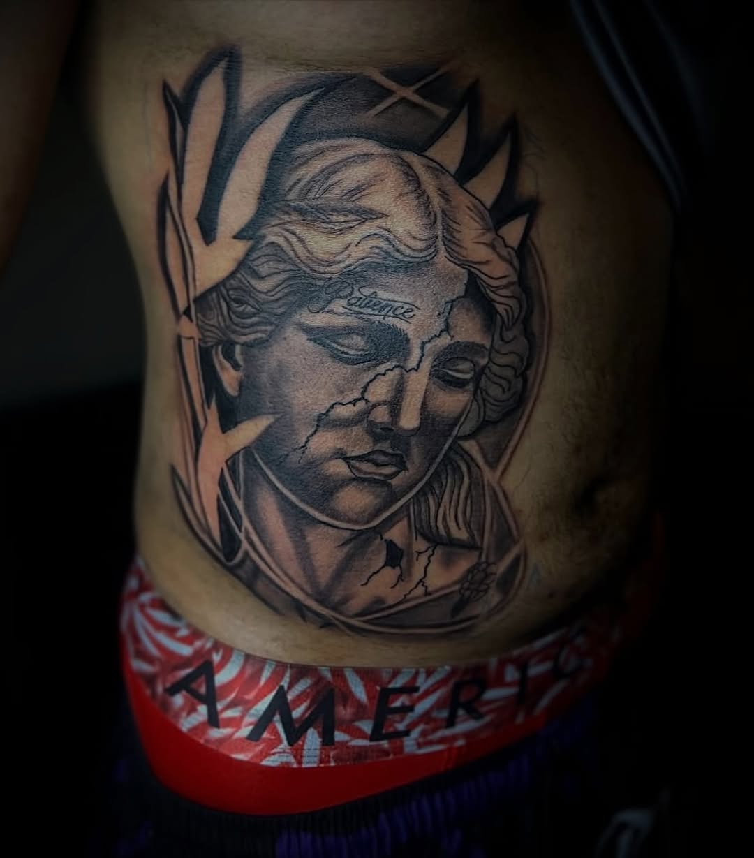 Cracked statue head with laurel wreath surrealism tattoo on the torso by @tattsbyleek