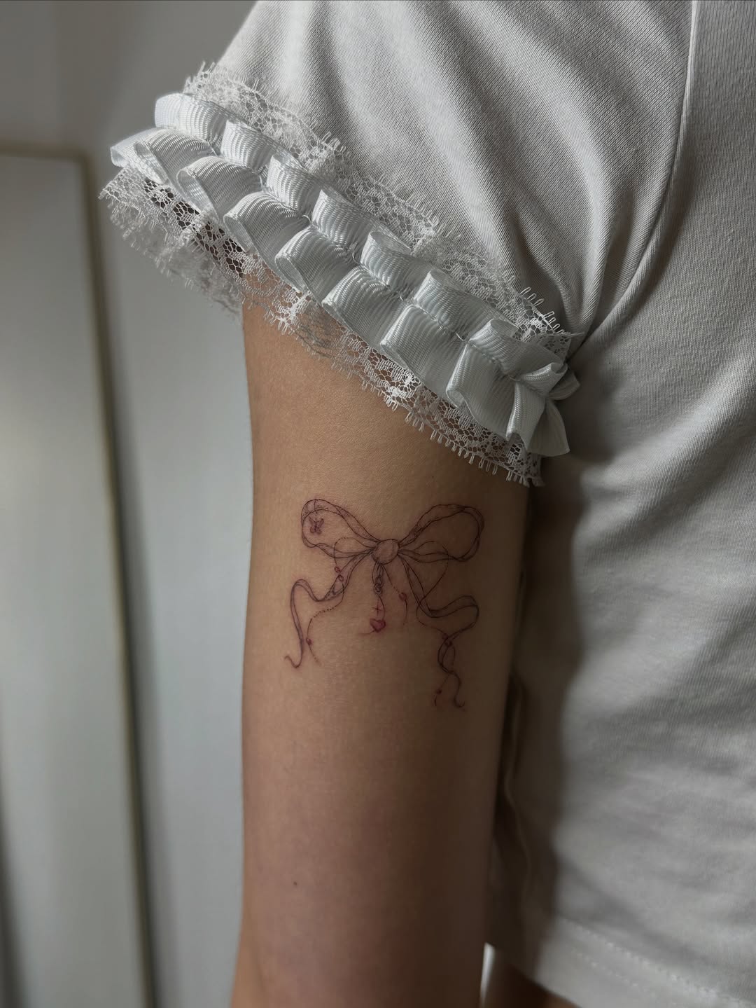 Bow with hearts minimalist tattoo on the forearm by @taravychi