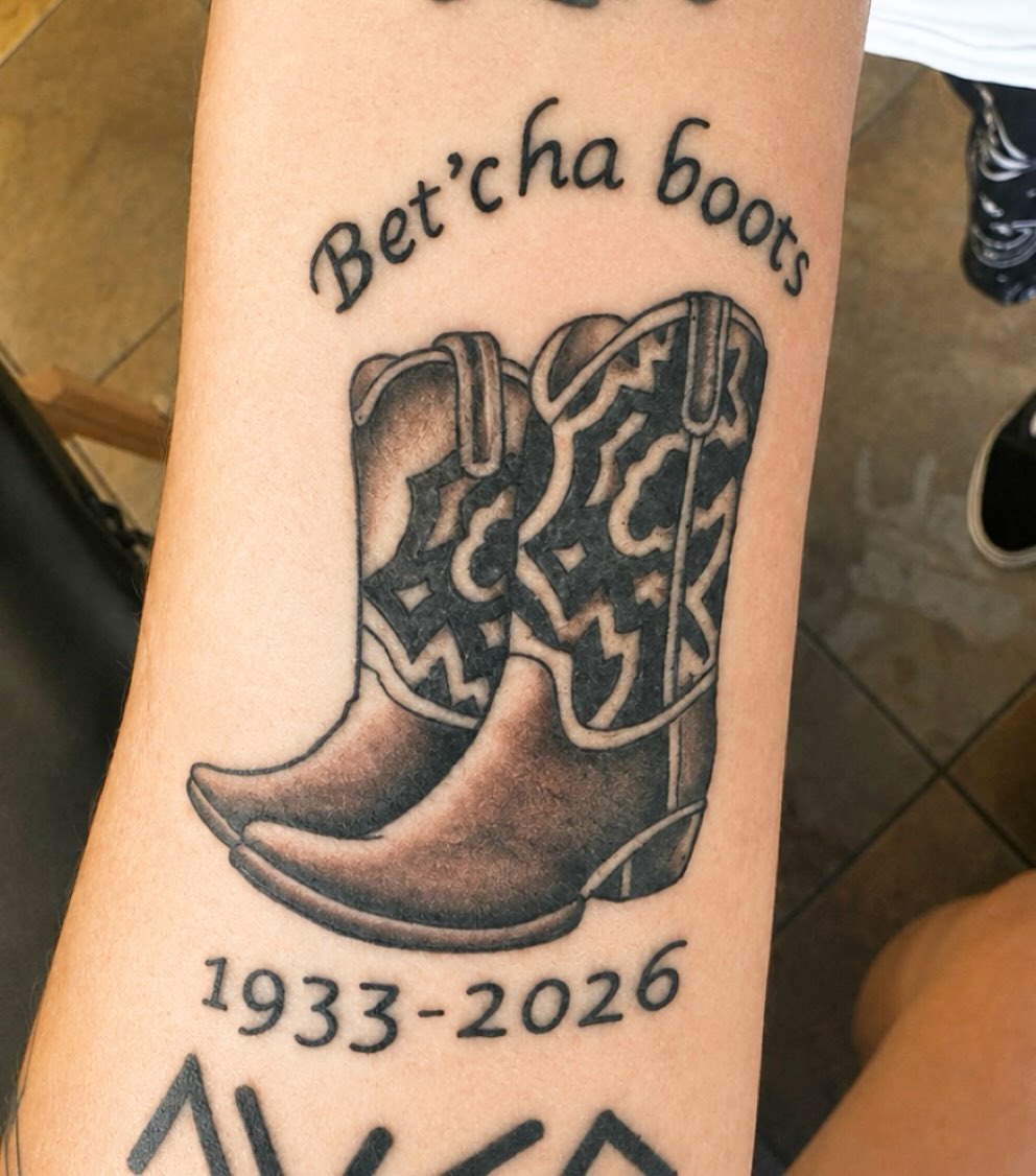 Cowboy boots with dates ignorant tattoo on the forearm by Stoney