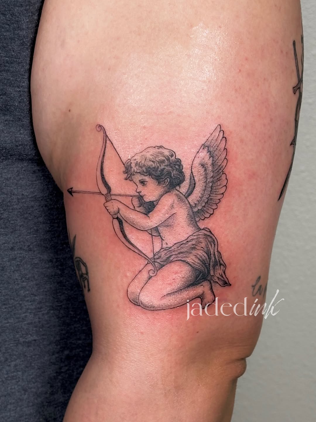 Cherub with bow and arrow ignorant tattoo on the thigh by 𝑱𝒂𝒅𝒆𝒅 𝑰𝒏𝒌 𝑷𝒆𝒓𝒎𝒂𝒏𝒆𝒏𝒕 𝑴𝒂𝒌𝒆𝒖𝒑 & 𝑻𝒂𝒕𝒕𝒐𝒐