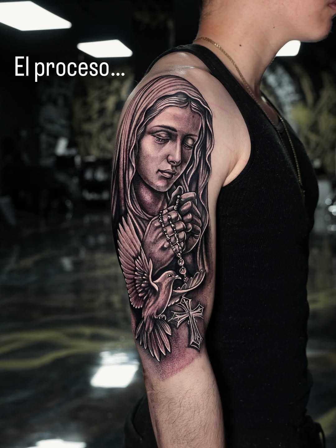 Virgin Mary with dove and cross Chicano tattoo on the upper arm by Alejo Ibanez Tattoo