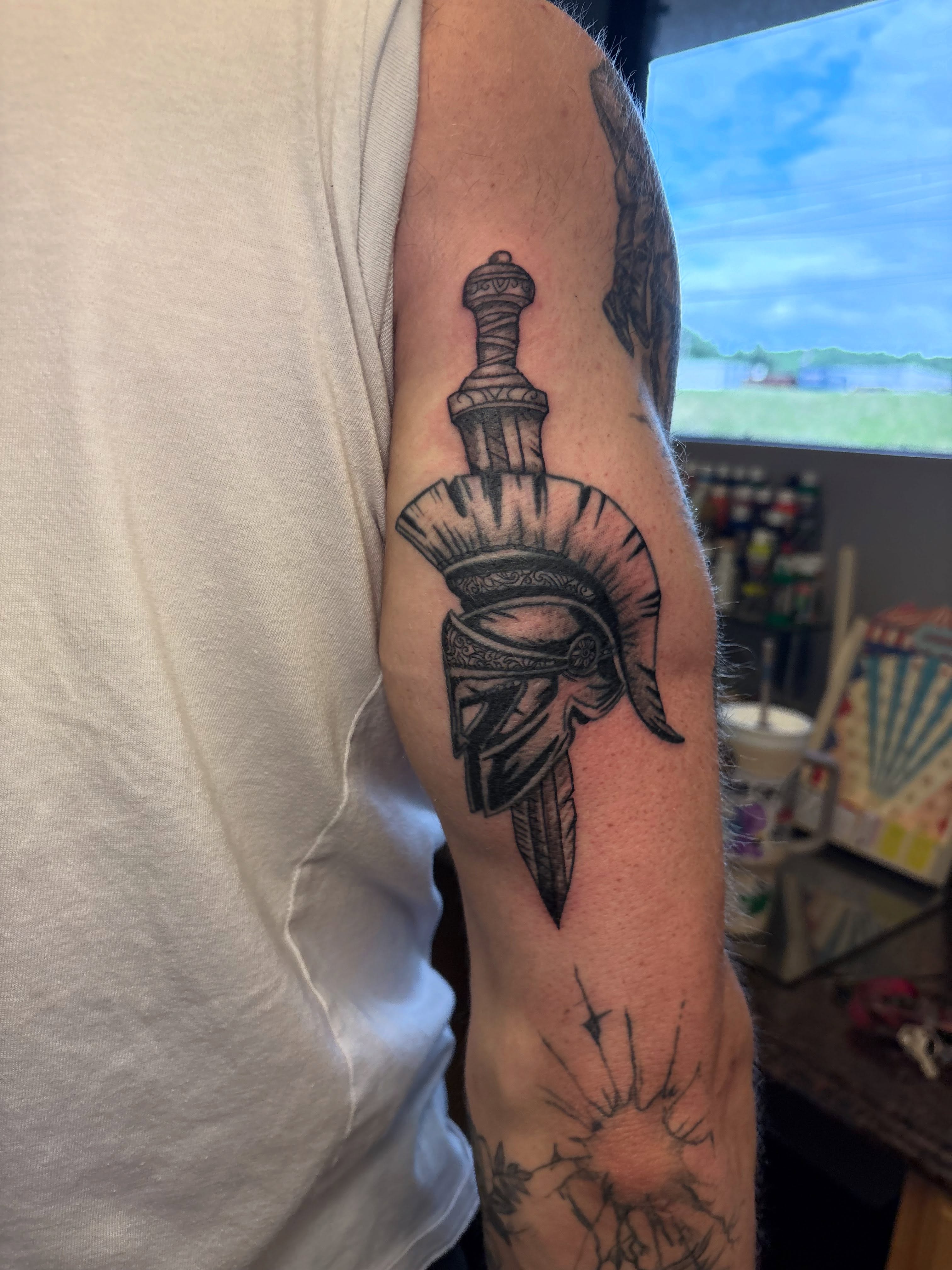 Spartan helmet and dagger black and grey tattoo on the forearm by Luke