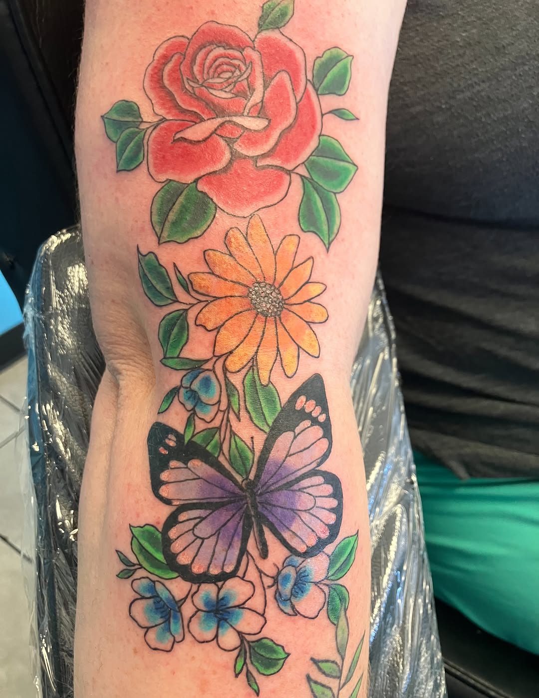 Rose, daisy, butterfly, and flowers neo-traditional tattoo on the forearm by Bryant Johnson
