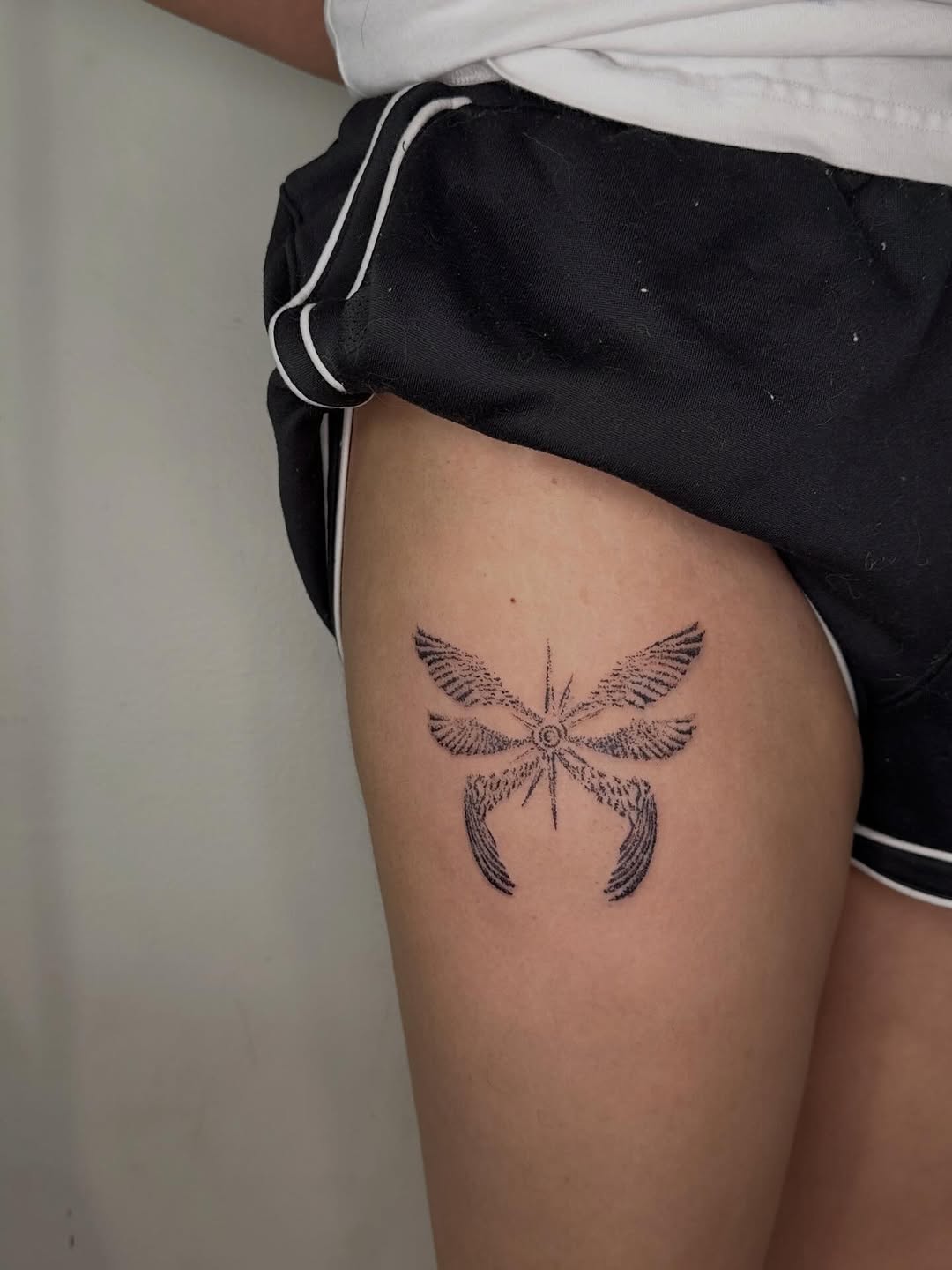 Stylized dragonfly with wings fine line tattoo on the thigh by Tomato