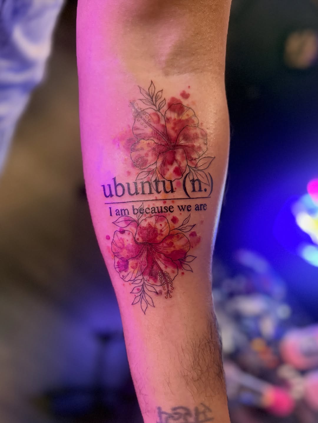 Ubuntu definition with hibiscus flowers tattoo on the forearm by Maggie George