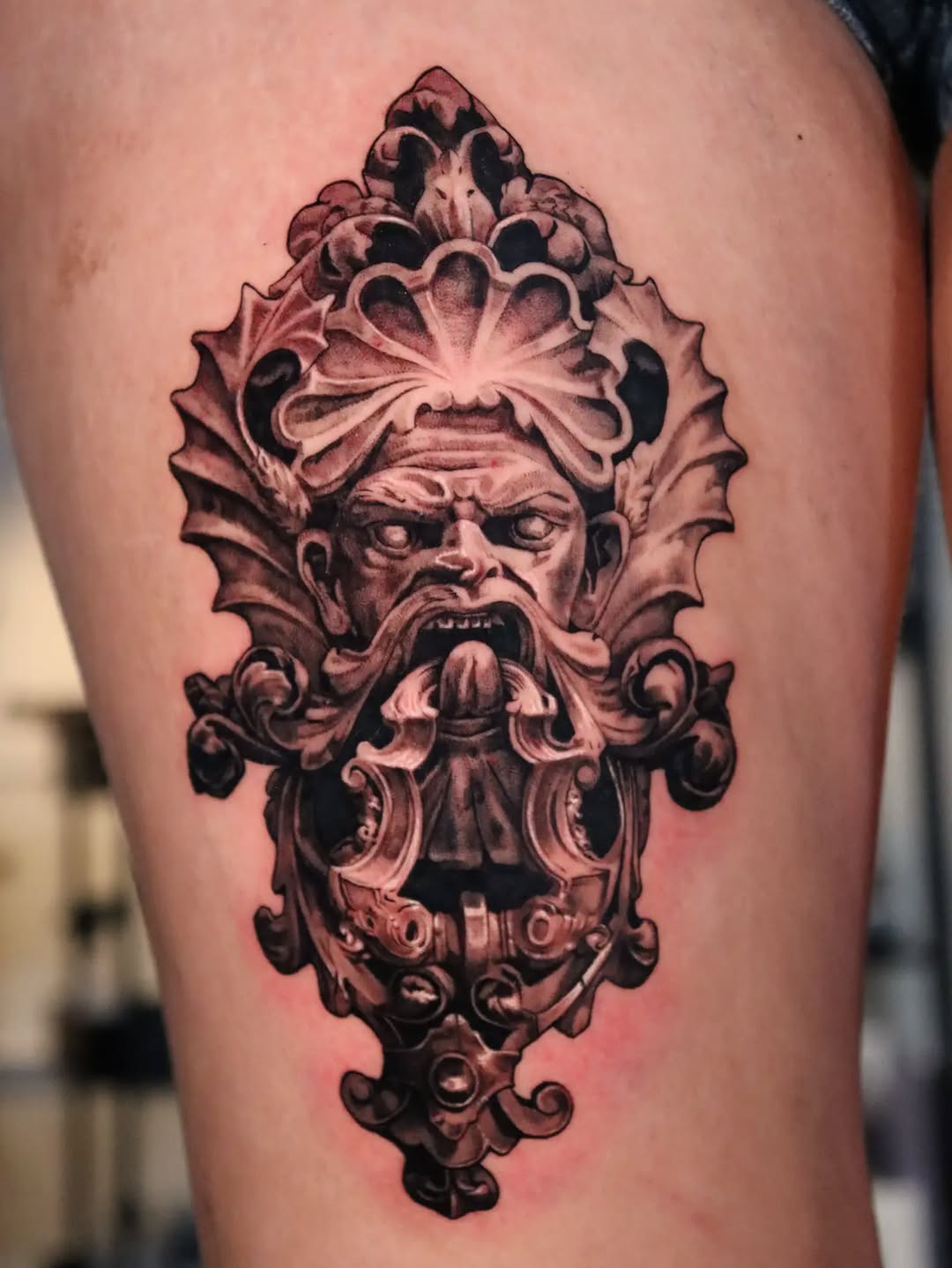 Gargoyle face with ornate frame surrealism tattoo on the thigh by Miami Florida Tattoo Artist