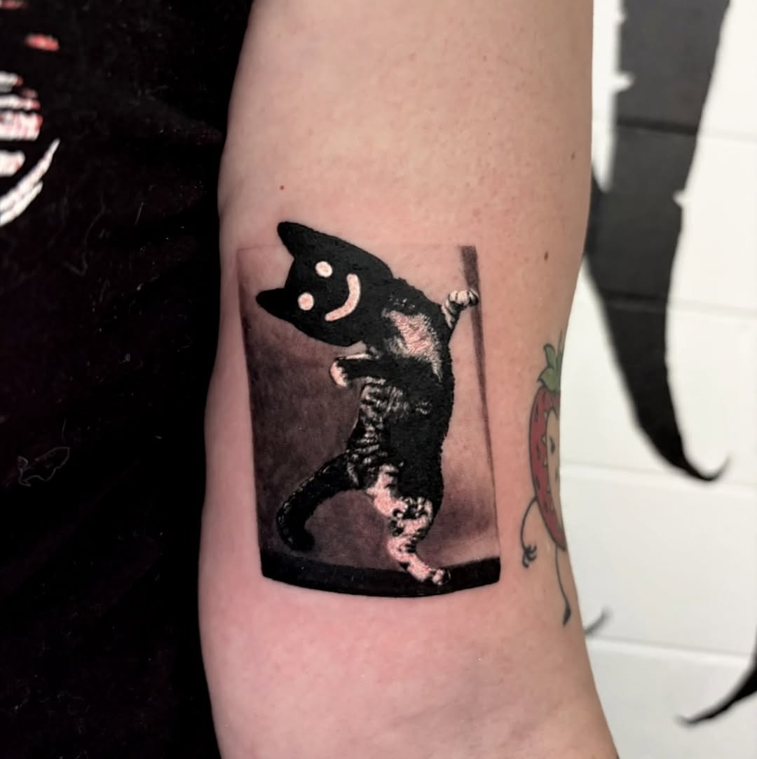 Dancing cat with smiley face realism tattoo on the forearm by @lil_stinker_5000, Portland, Oregon