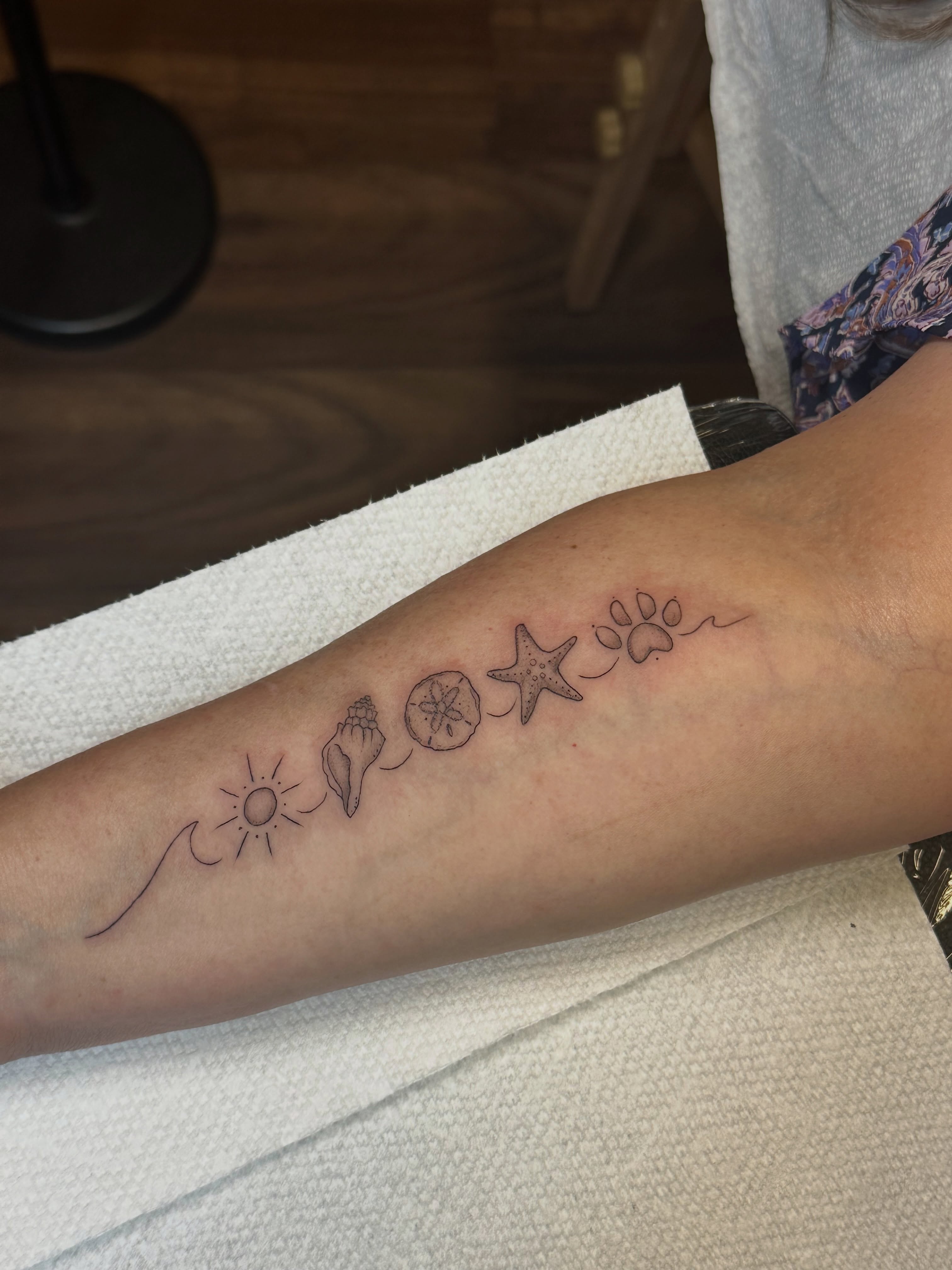 Beach-themed symbols black and grey tattoo on the forearm by Lauren