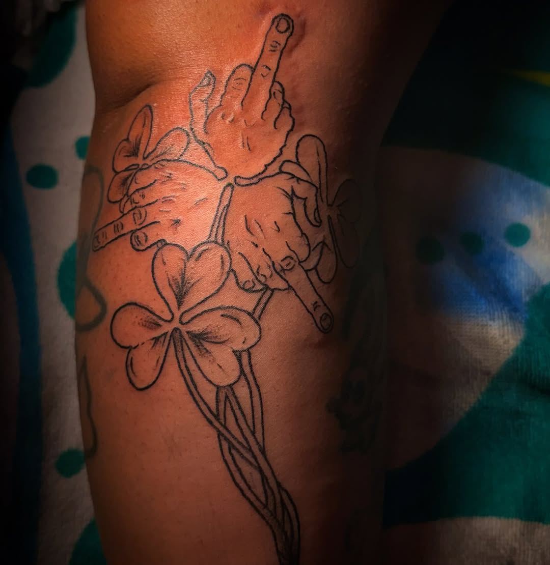 Hands giving middle finger with shamrocks tattoo on the thigh by RVA Tattoo Artist
