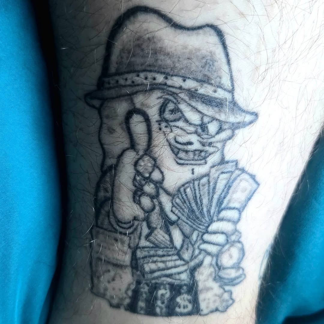 Cartoon character with hat and money ignorant tattoo on the forearm by π«