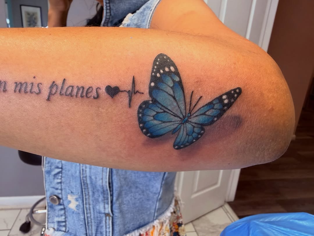 Blue butterfly with lettering fine line tattoo on the forearm by linda perez