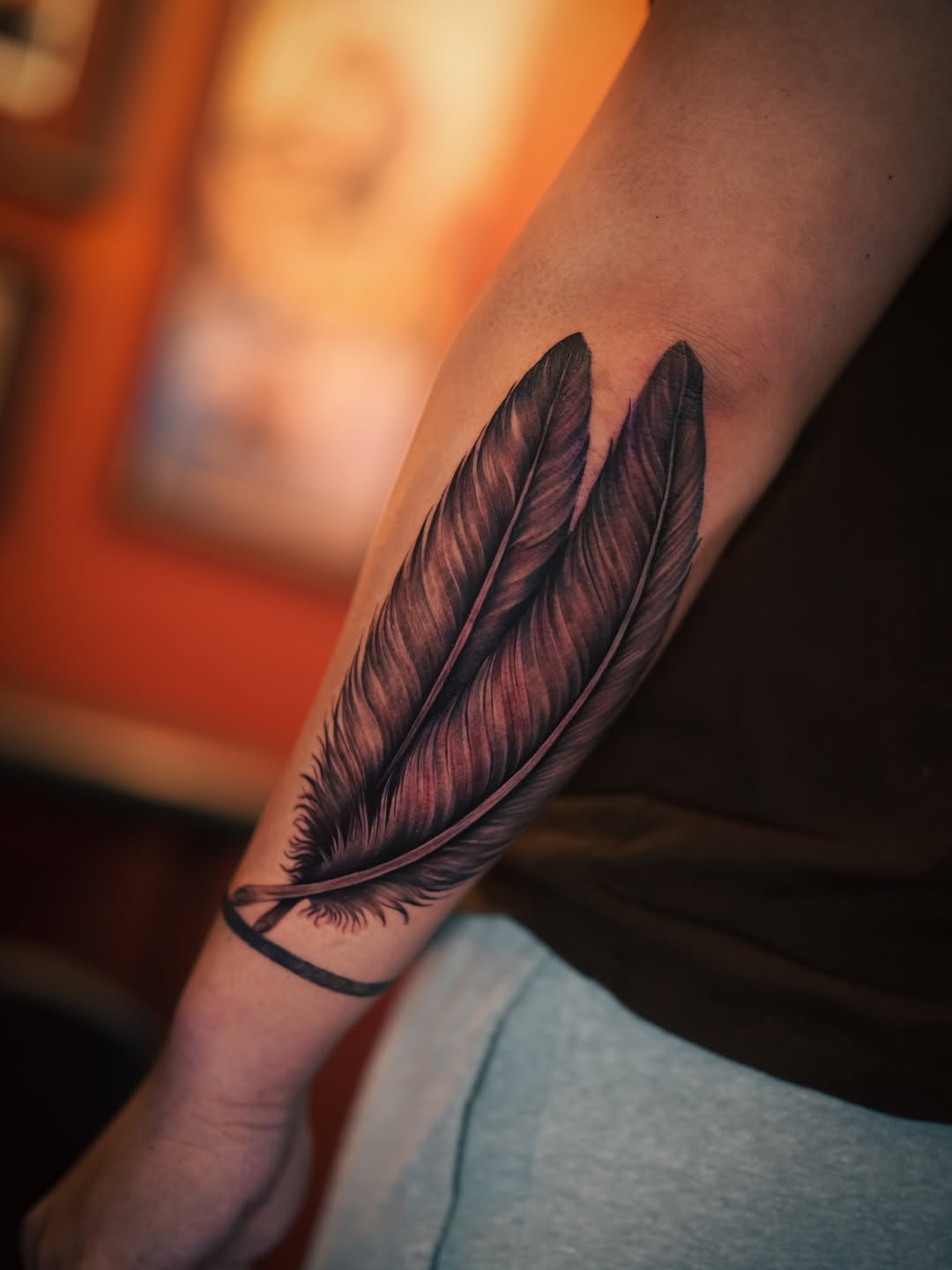 Two feathers with band fine line tattoo on the forearm by Franz Muñoz