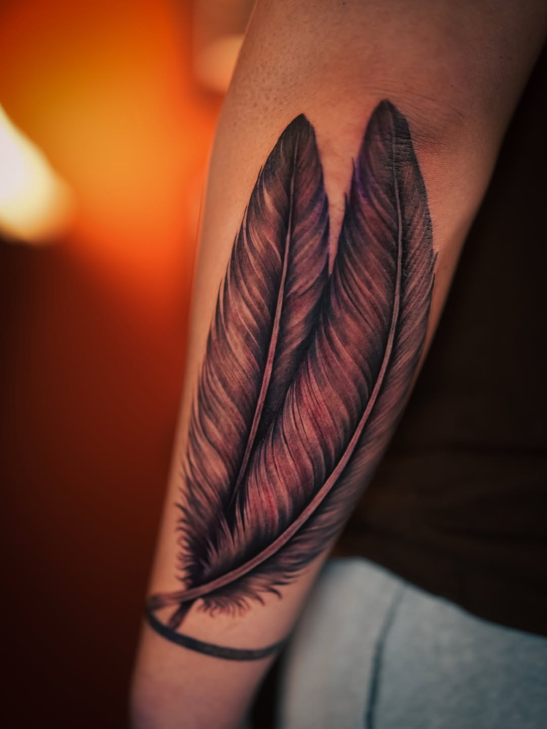 Two feathers fine line tattoo on the forearm by Franz Muñoz
