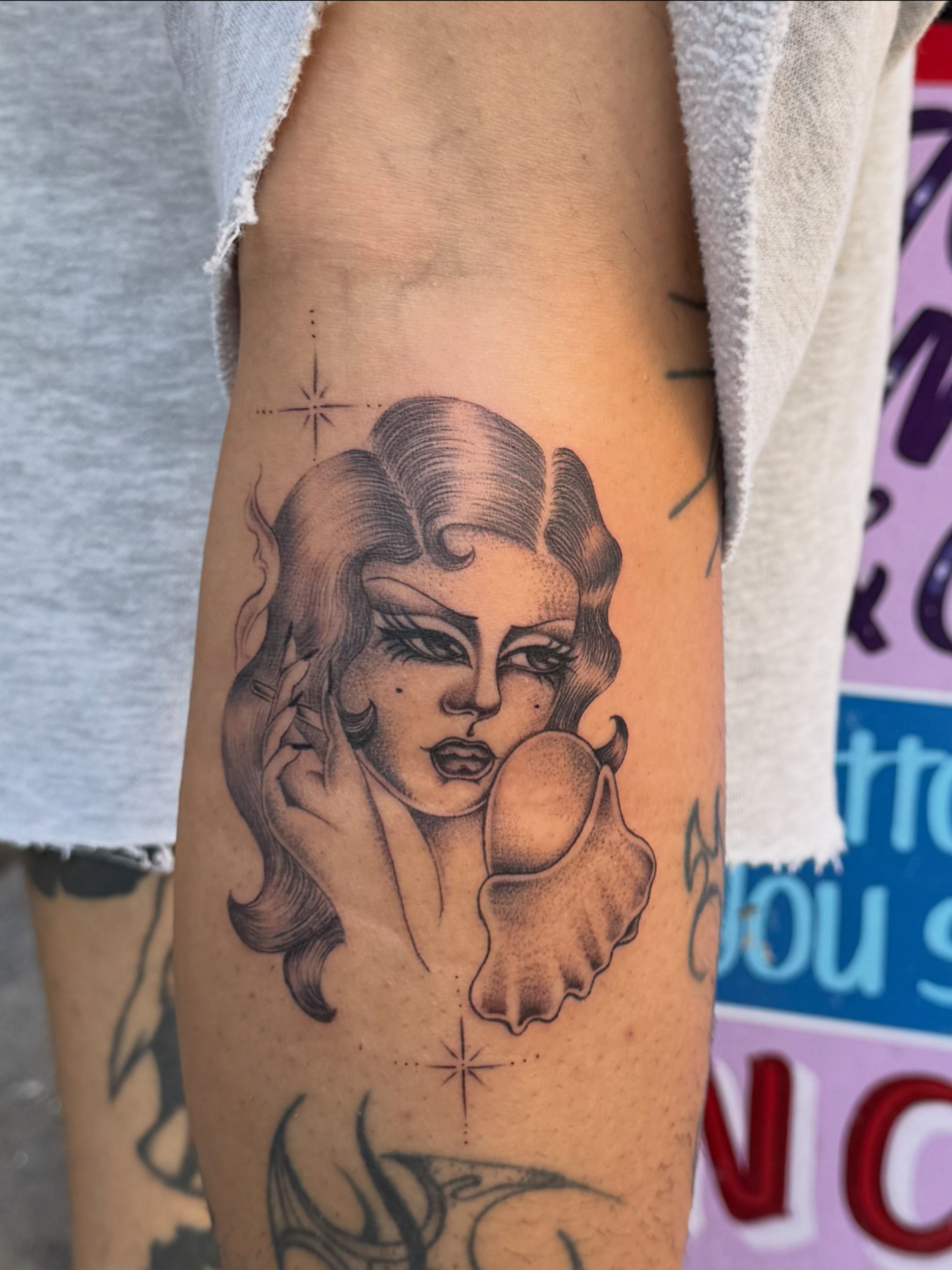 Woman holding shell black and grey tattoo on the forearm by H e I D I