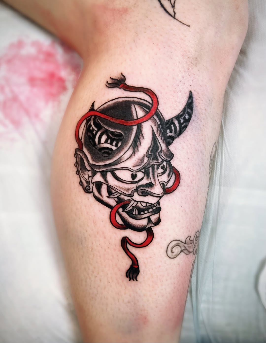 Oni mask with red rope Japanese tattoo on the thigh by Shay Cole
