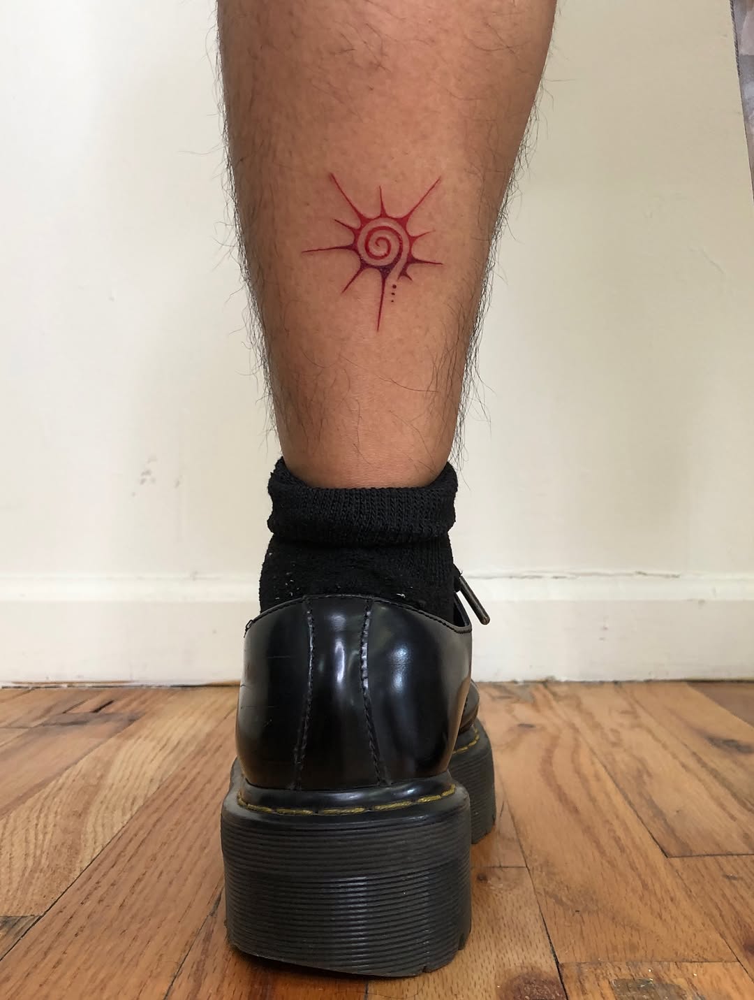Red spiral sun symbol tattoo on the calf by thalia